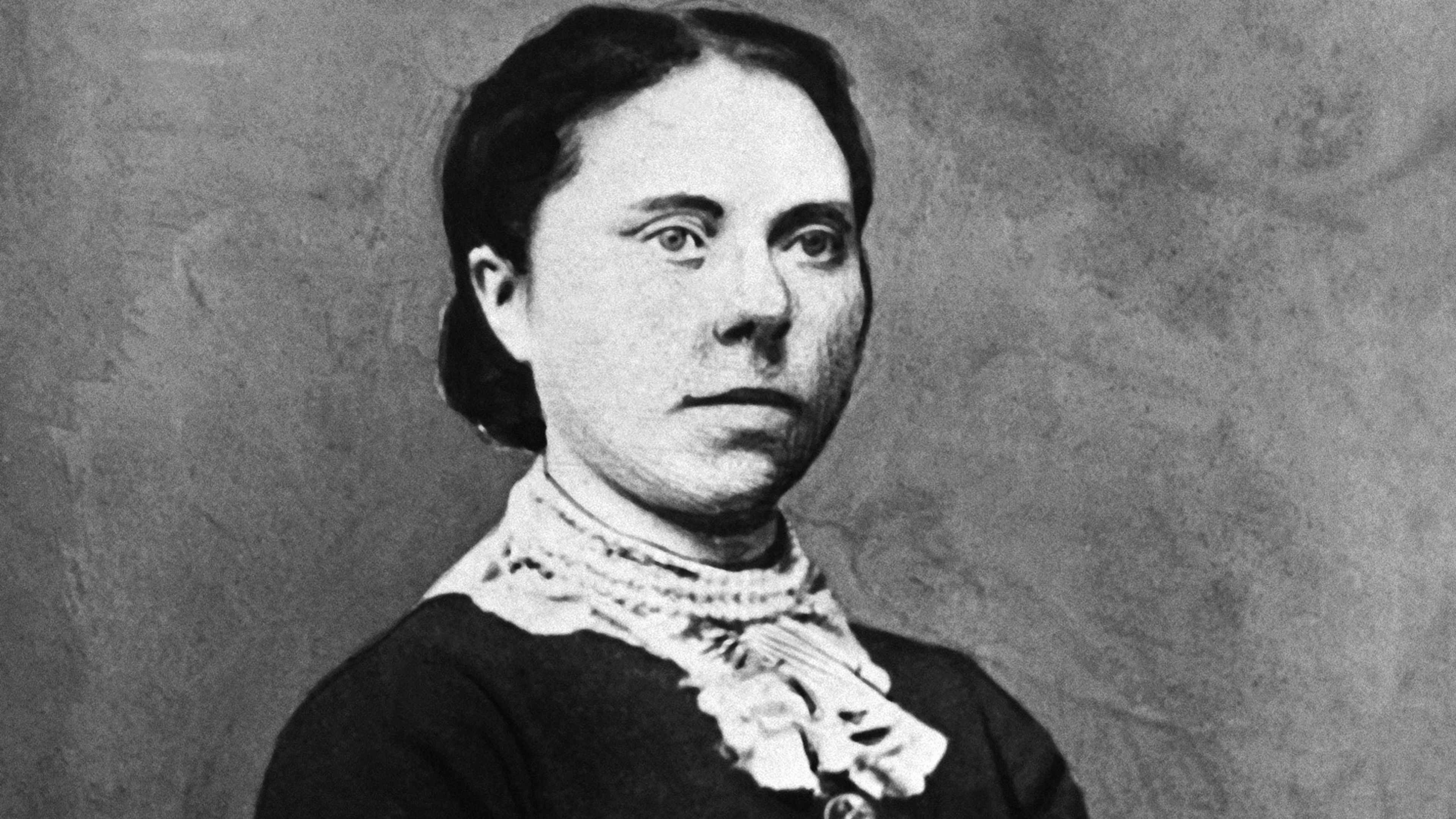 A black and white portrait of a serious-looking woman with dark hair and a lace collar, set against a plain background.
