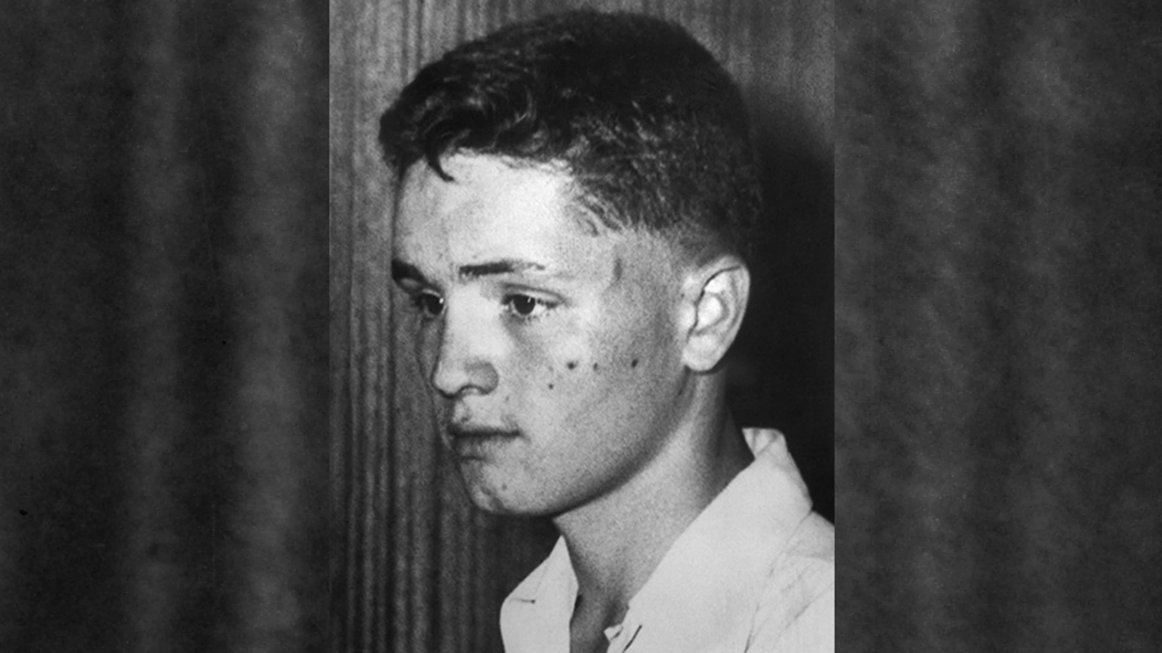 A black and white portrait of a young man with a serious expression, set against a dark background.