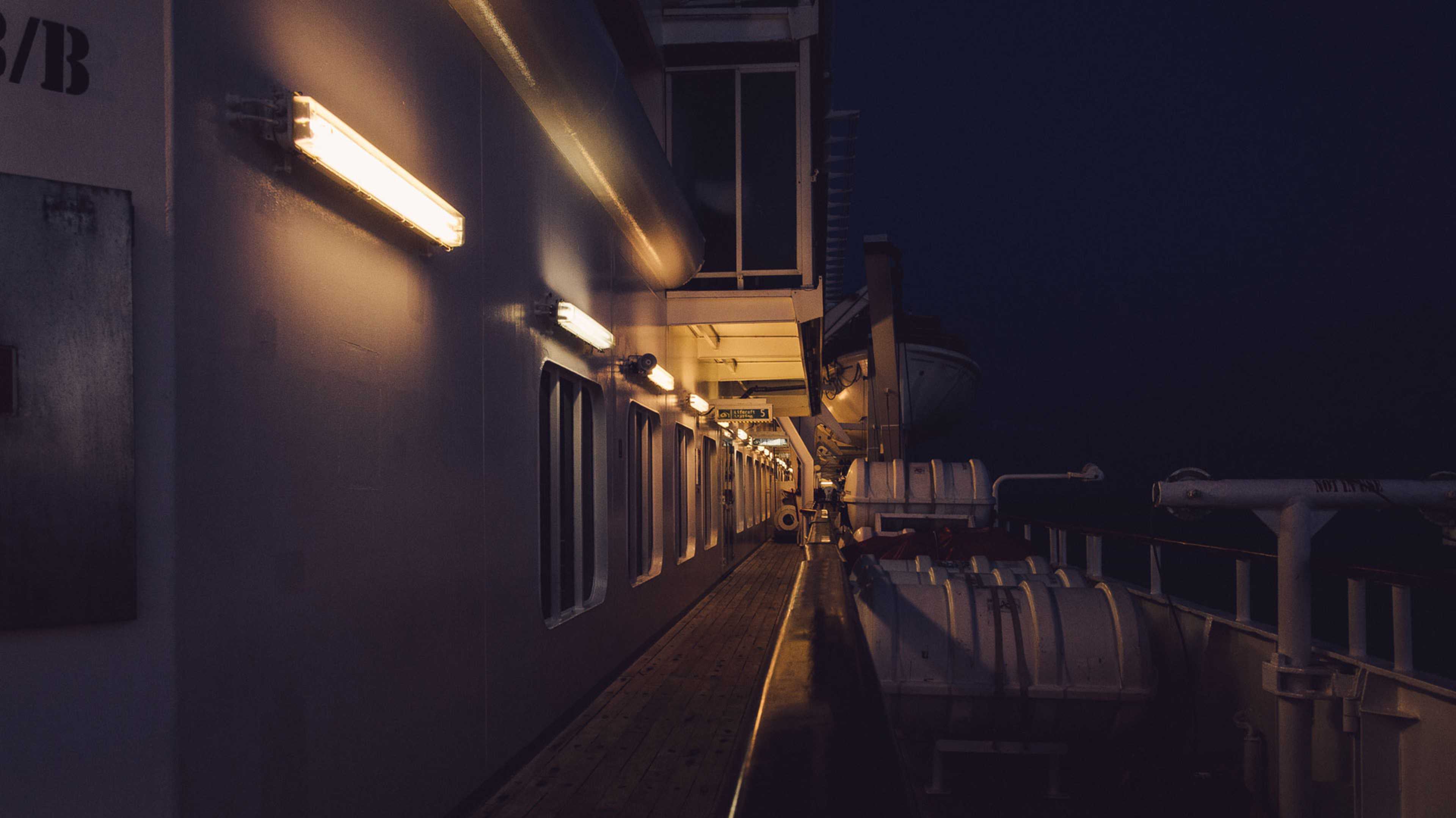 A dimly lit hallway with rows of lockers or storage units lining the walls, creating a sense of depth and leading the viewer's eye down the corridor.