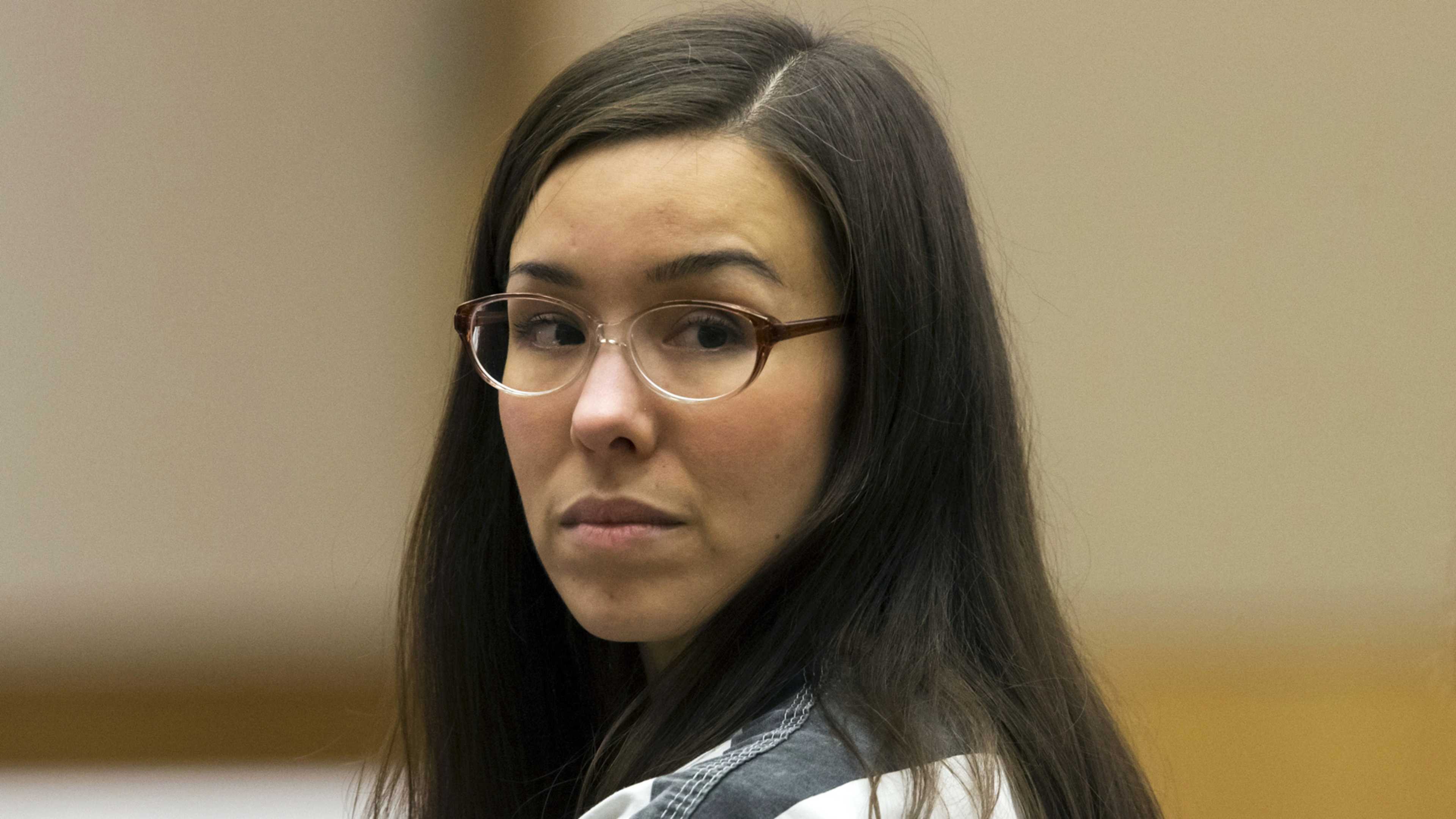 A young woman with long dark hair and glasses, wearing a neutral expression, is the focal point of the image, which appears to be set in a professional or office-like environment.