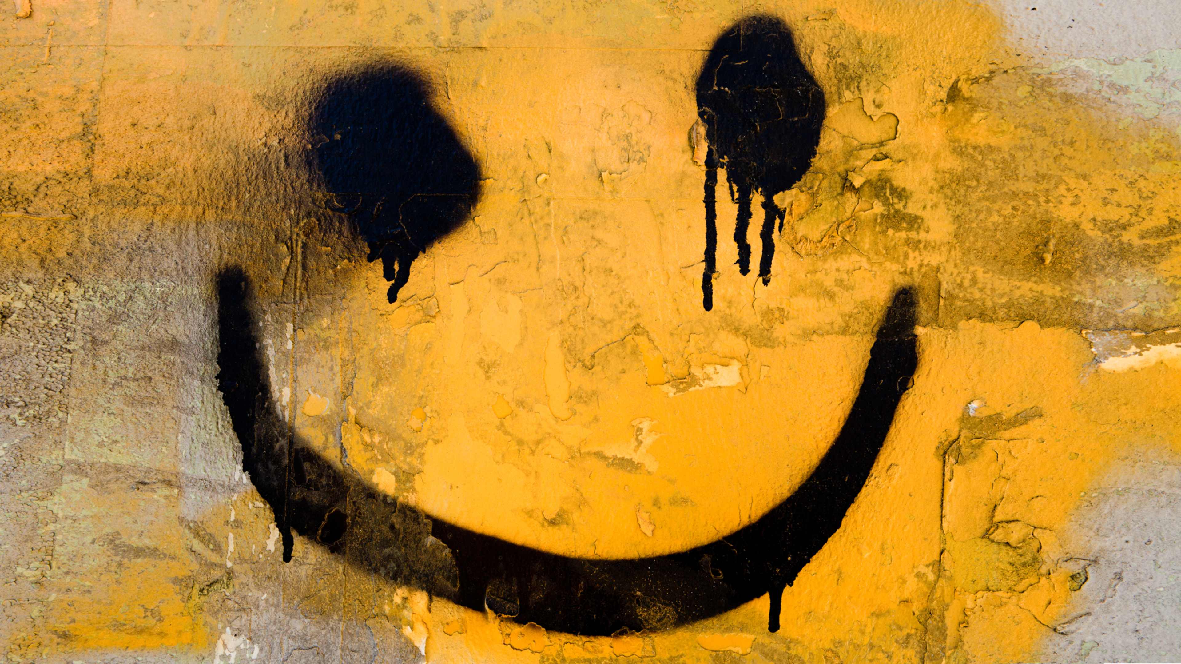 A large, stylized smiley face with dripping black paint or ink against a textured, golden-yellow background.