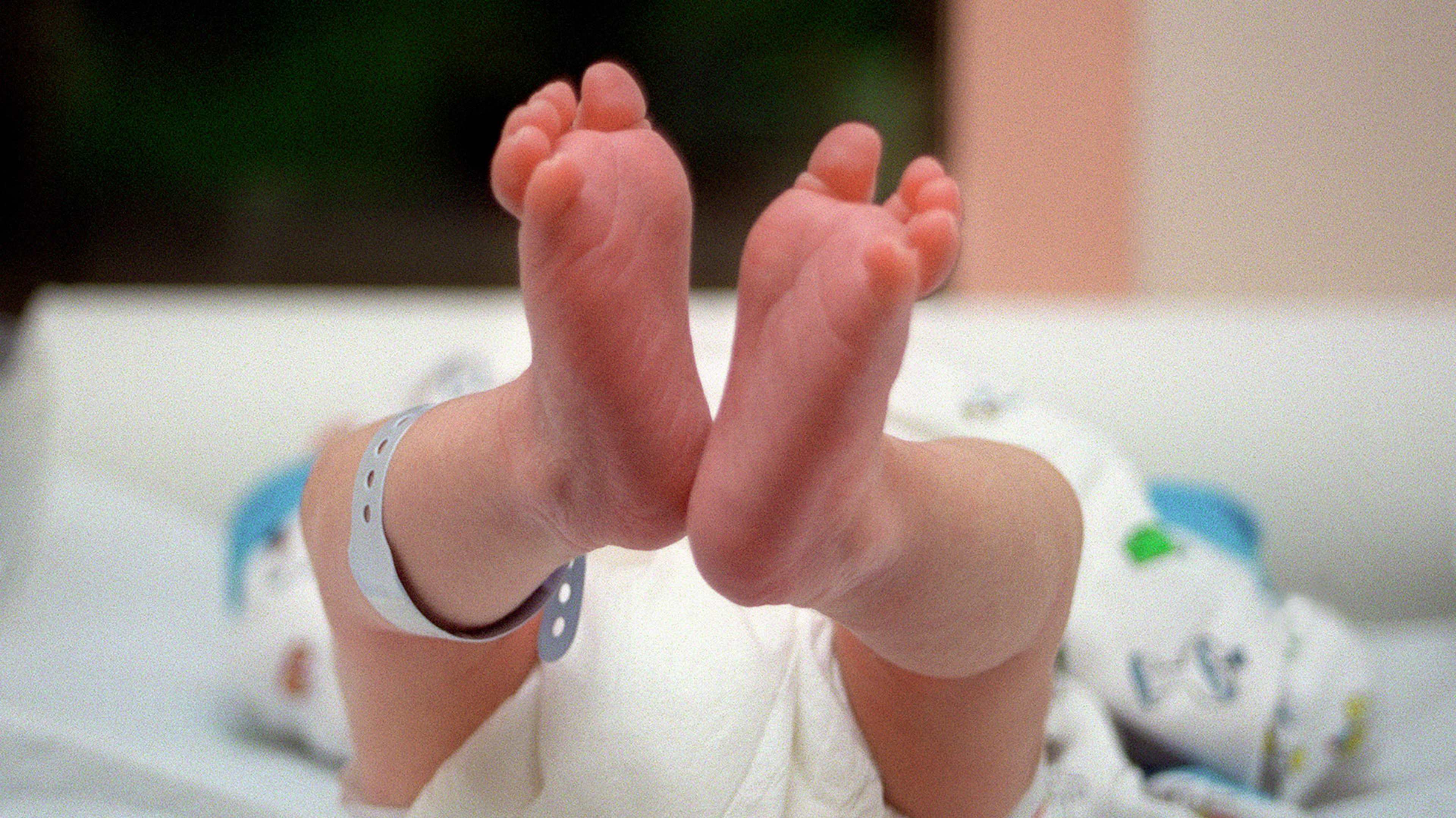 The image shows a pair of bare feet resting on a white surface, with a colorful patterned background visible behind them.