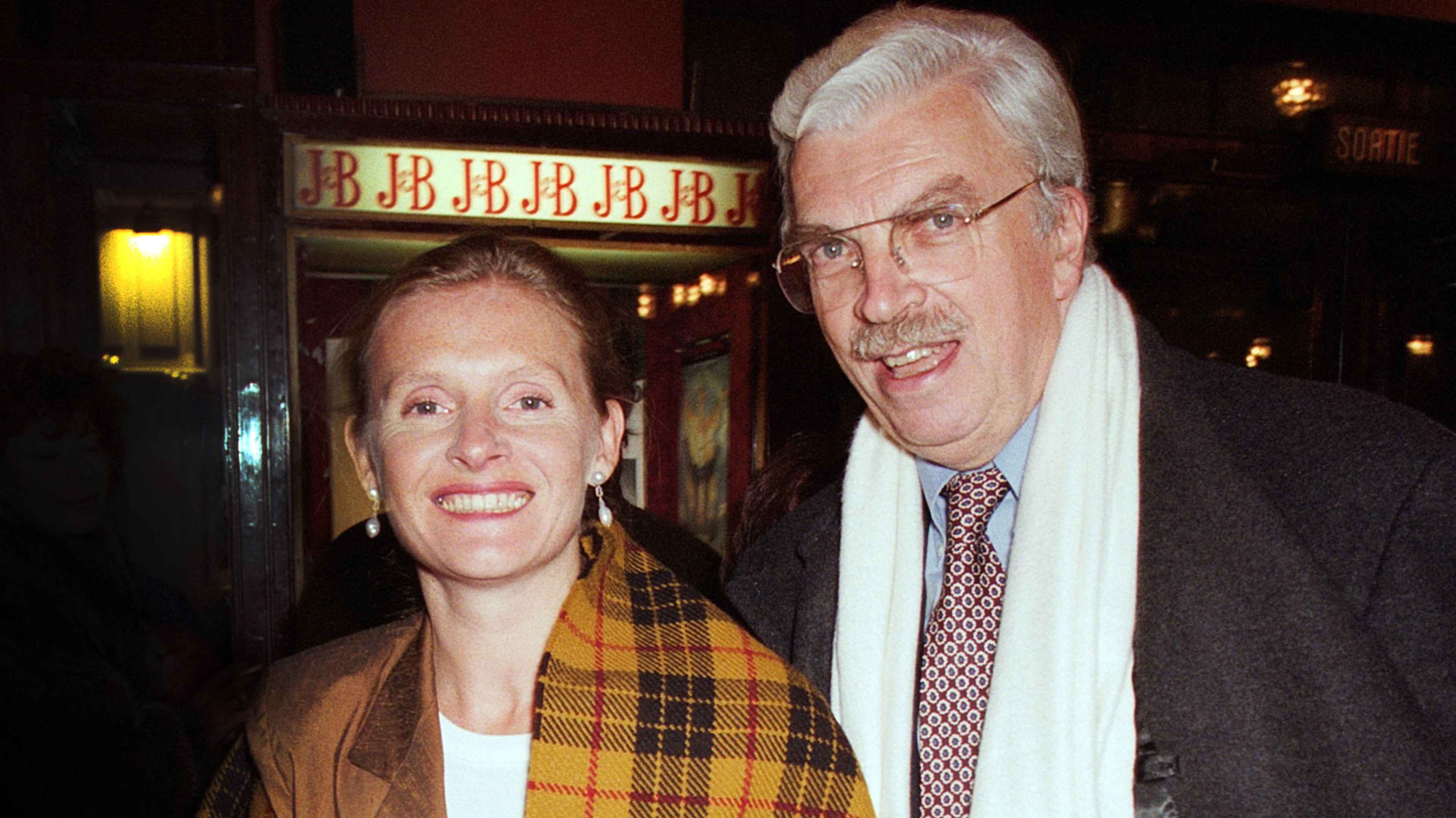 The image shows an older couple, a man and a woman, standing together and smiling in front of a theater marquee with the word "BBBBB" displayed.