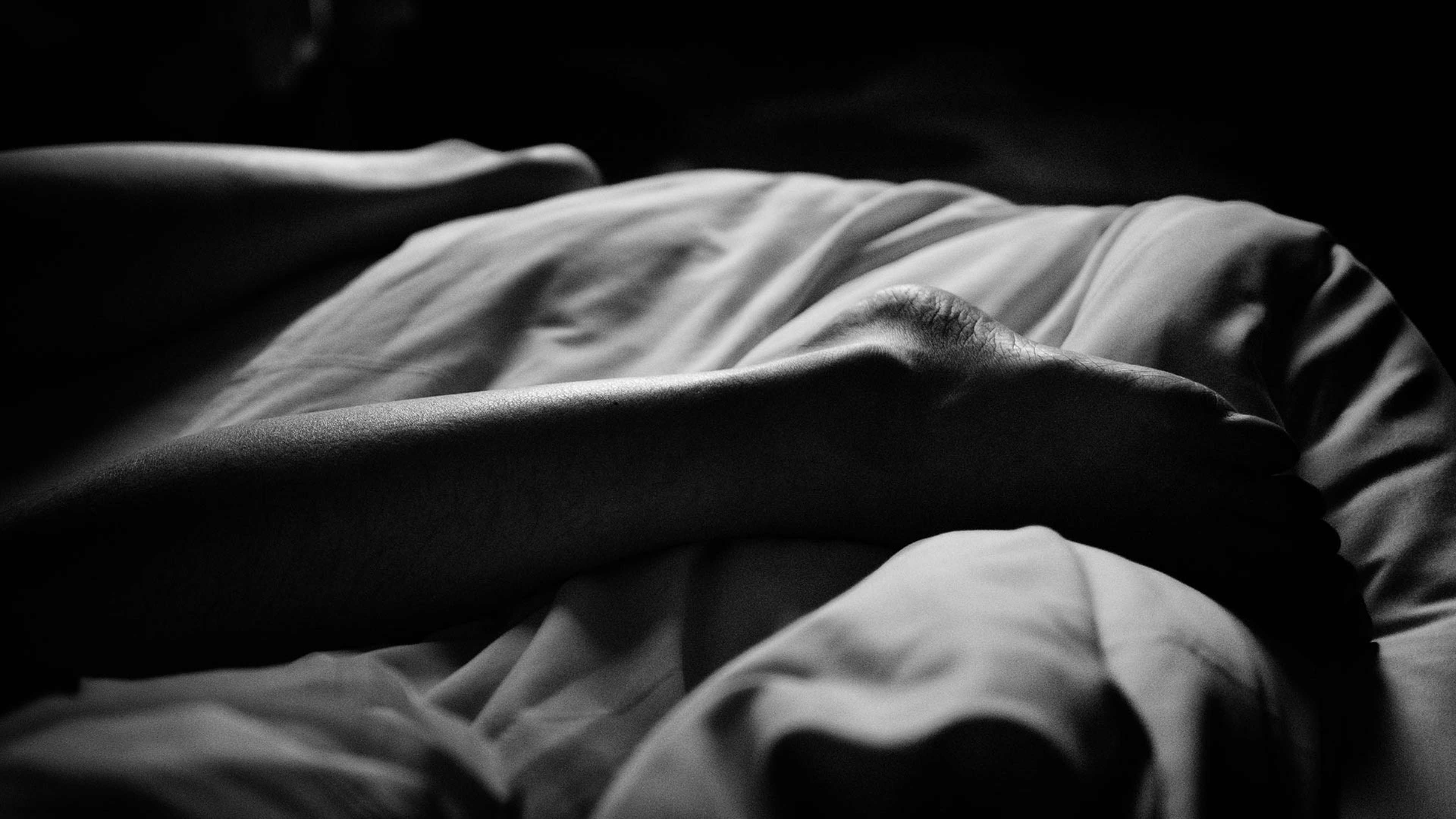 A close-up, black and white image of a person's face partially obscured by fabric, creating a sense of mystery and introspection.