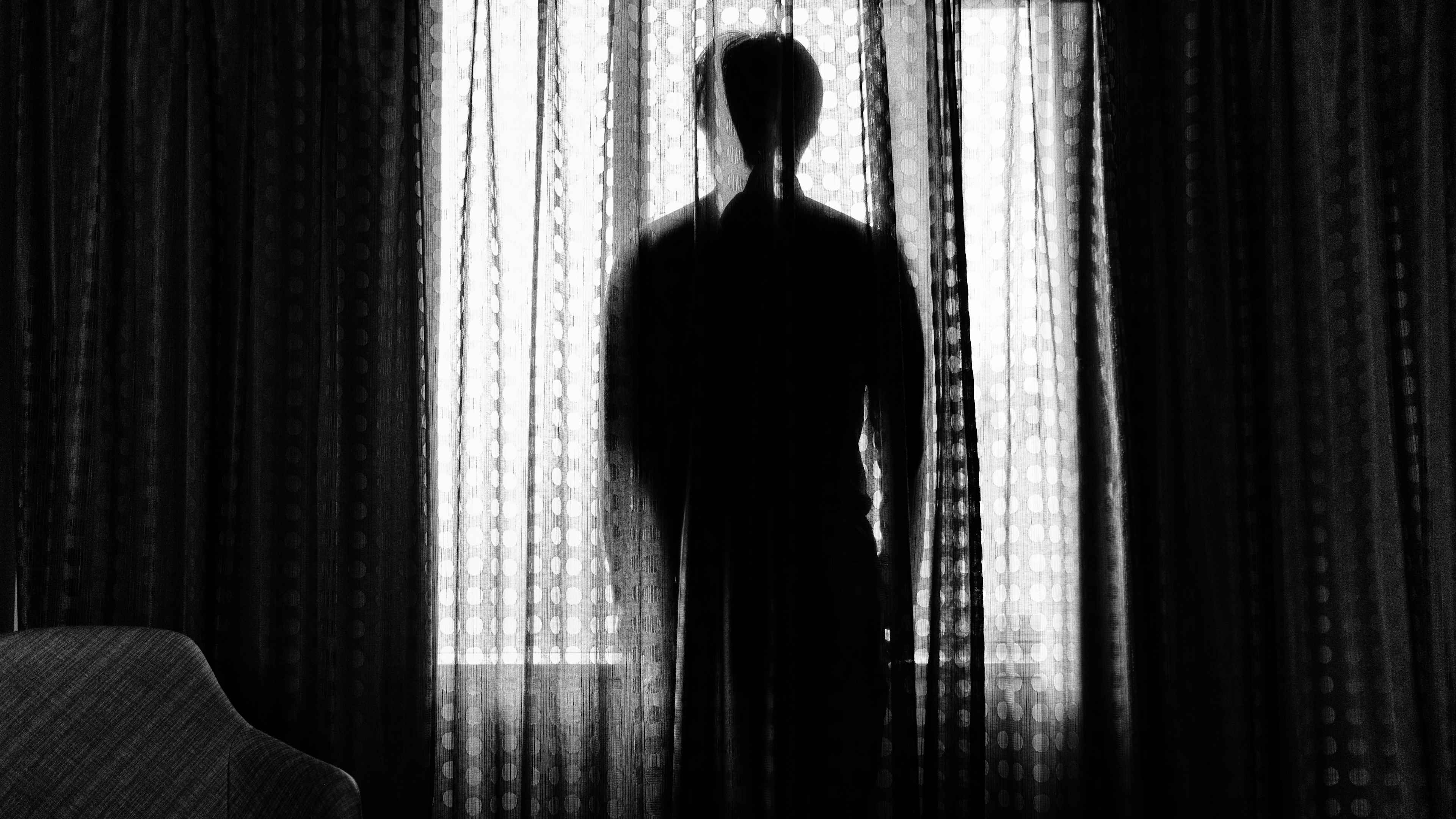 Image of a suspicious figure hiding behind a polka dot lace curtain