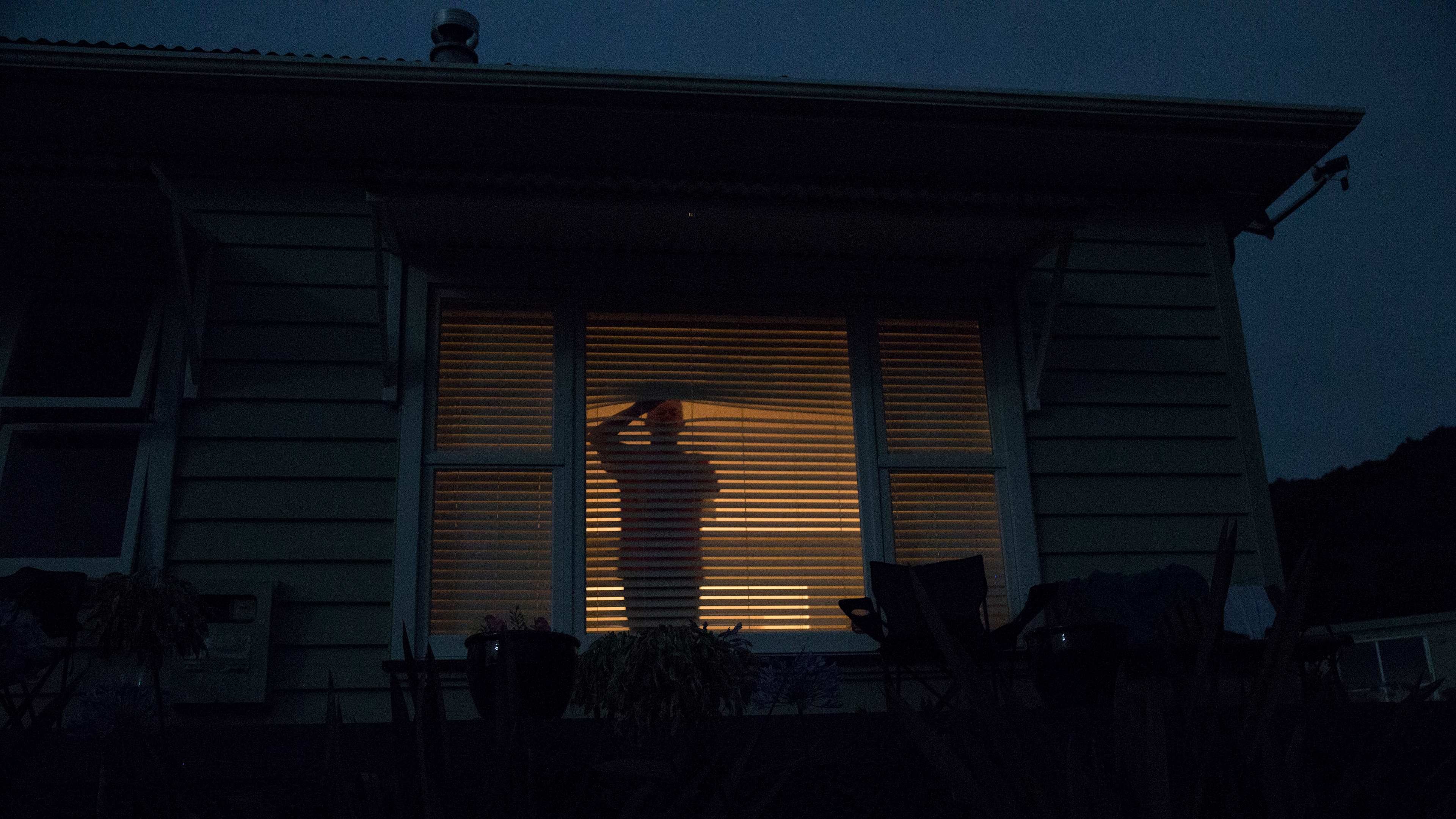 Silhouette of a person standing behind a window with blinds at night, Northland, New Zealand