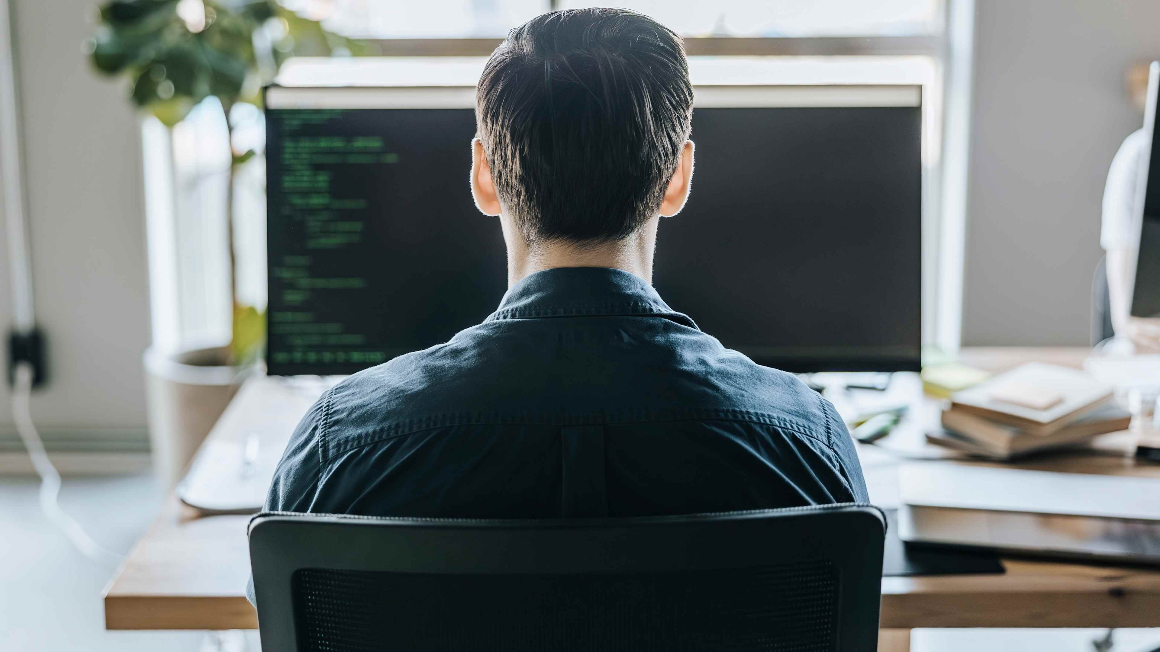 Rear view of male programmer coding while sitting at desk in tech startup office