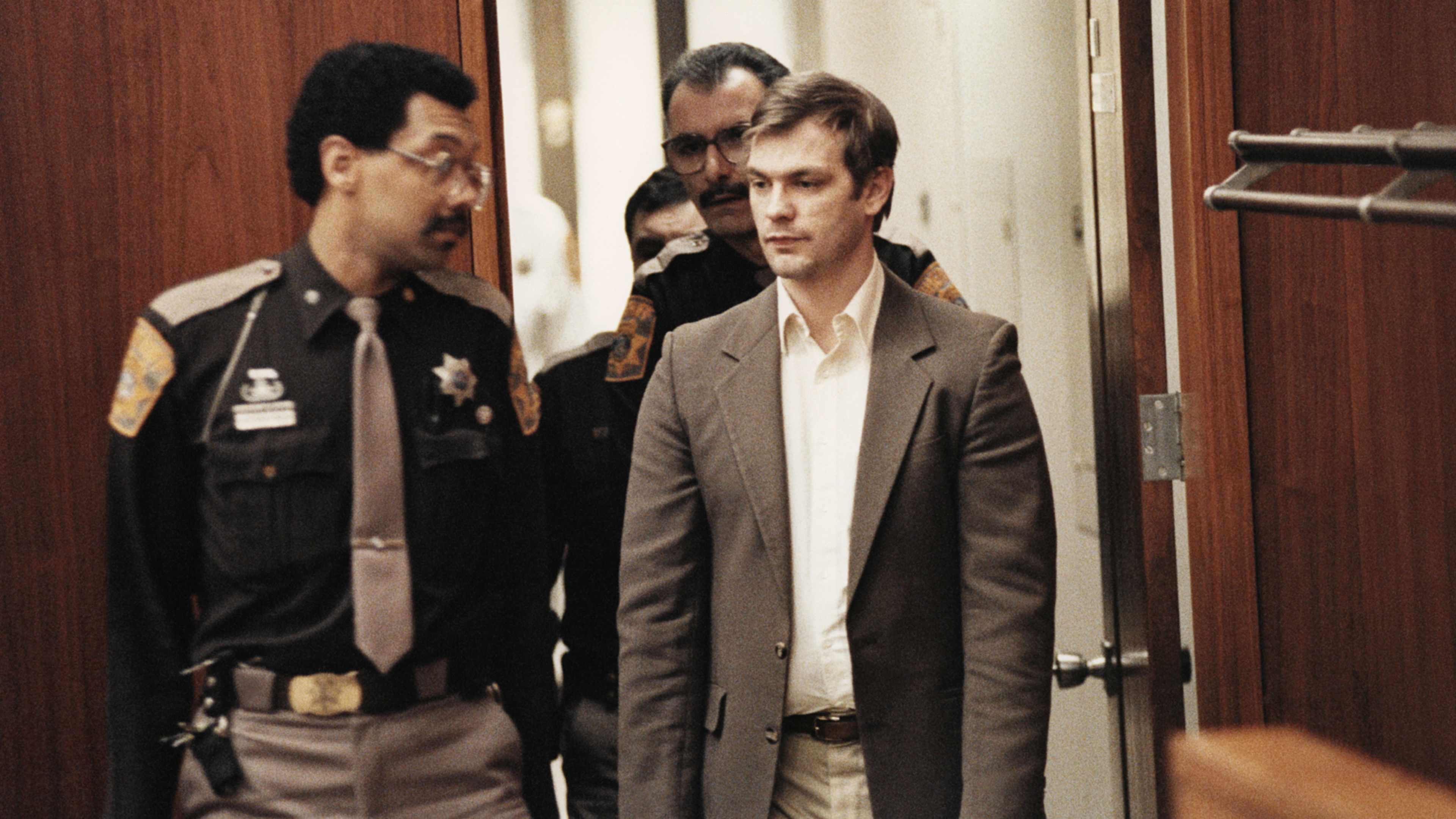 Two men, one wearing a police uniform and the other in a suit, are standing in a doorway.