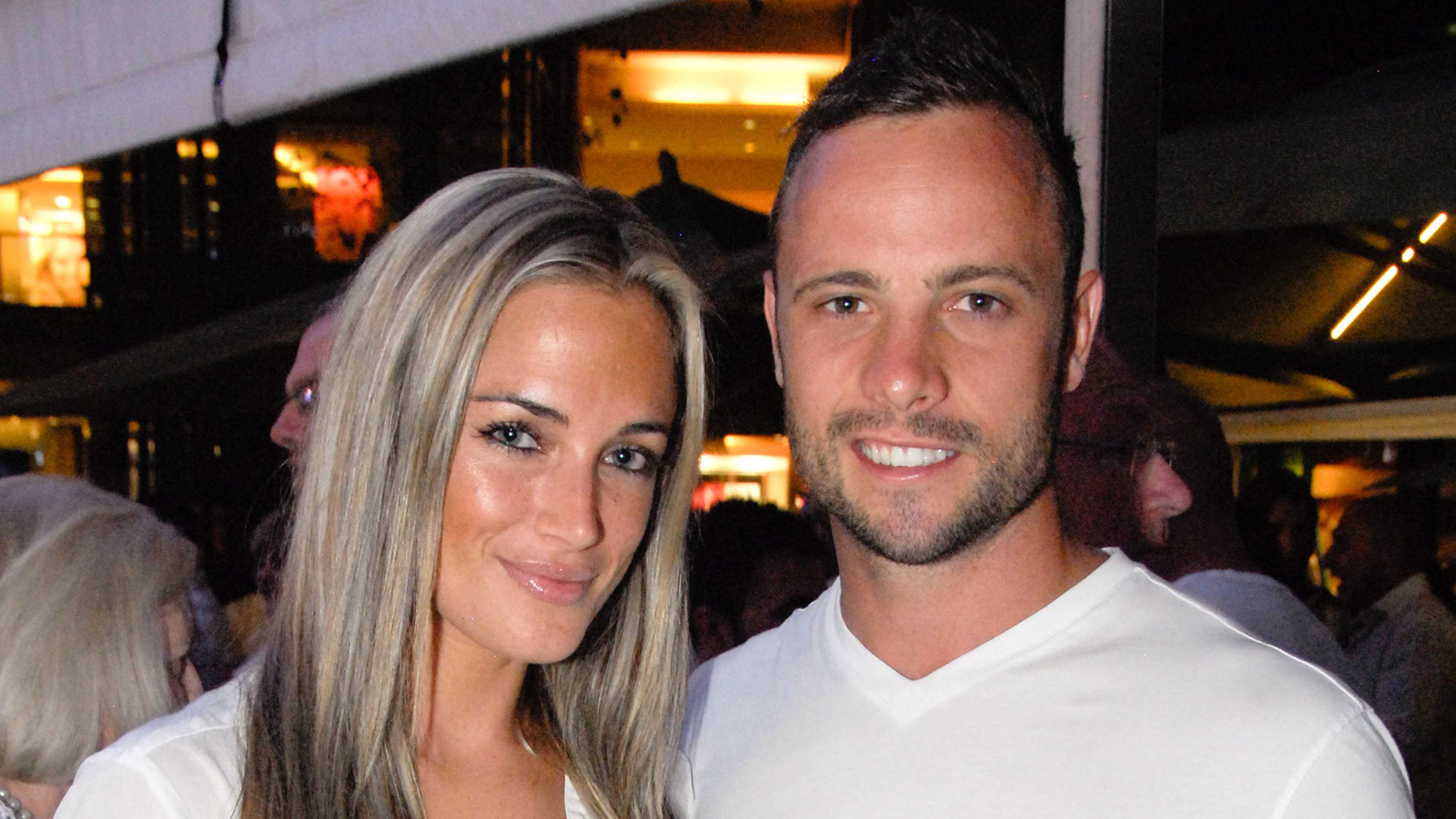 The image shows a smiling couple posing together in what appears to be a restaurant or bar setting, with warm lighting and a blurred background.