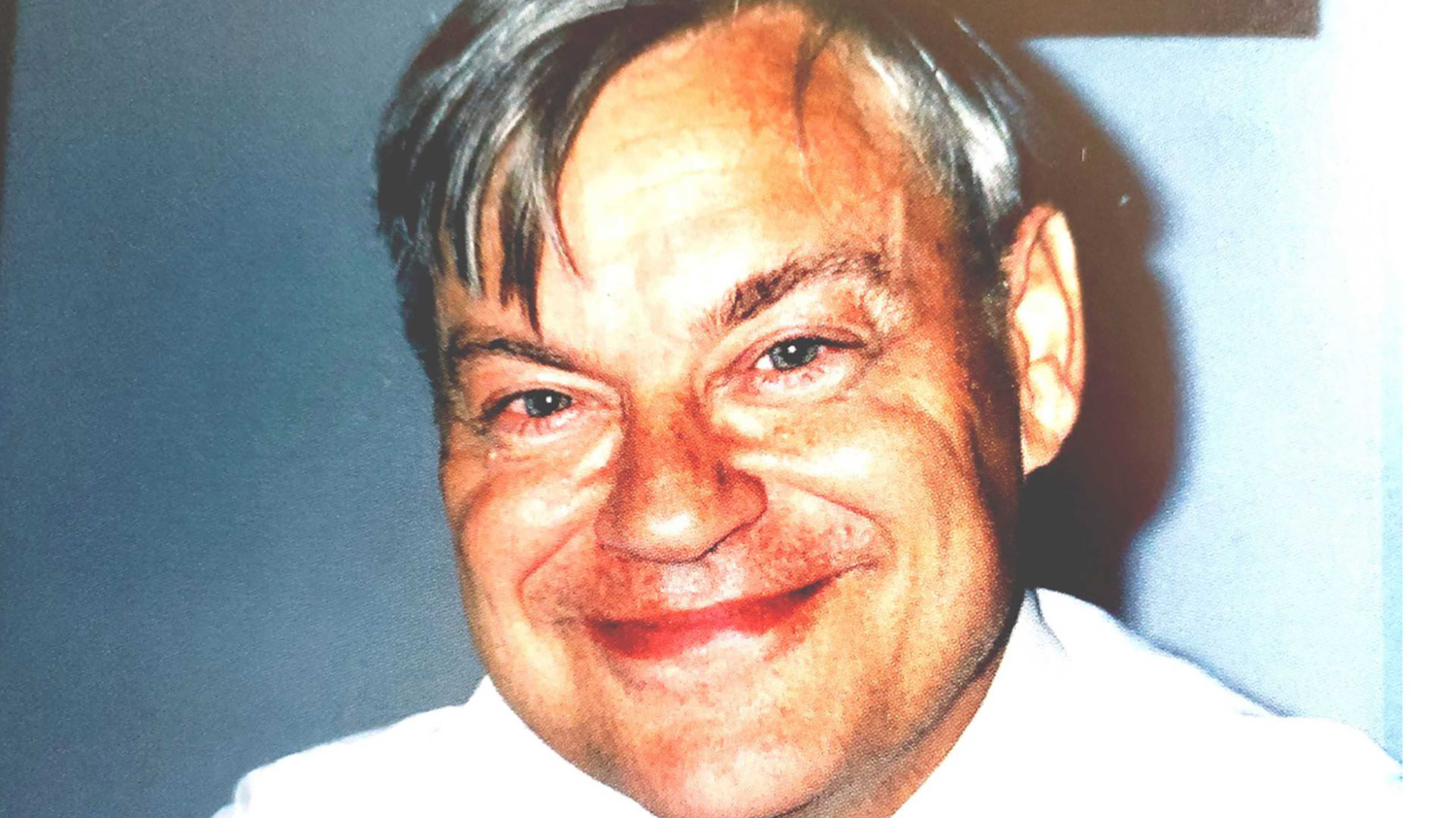 The image shows a close-up portrait of a smiling older man with gray hair and a friendly expression.