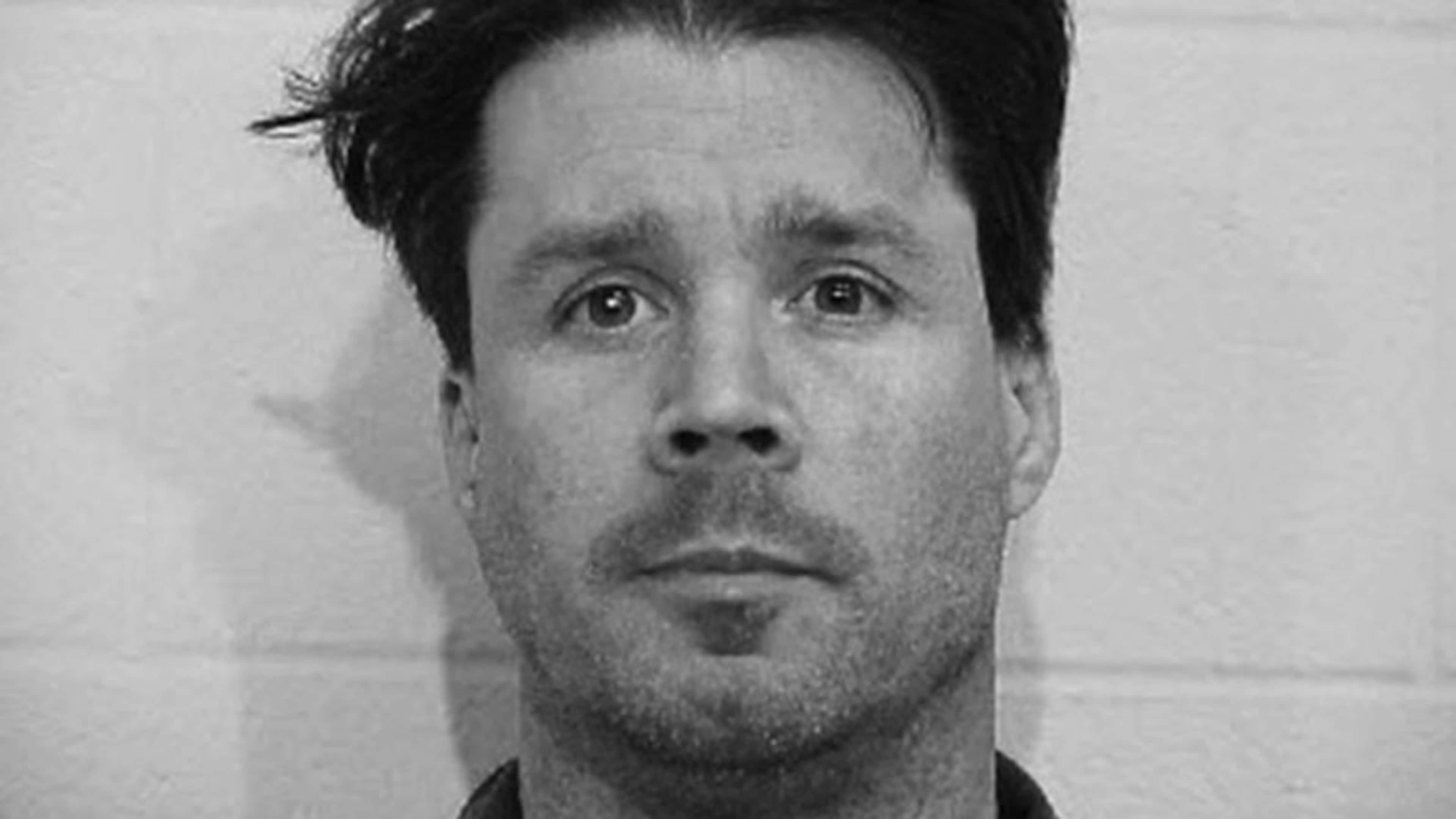 A black and white close-up portrait of a man with a serious expression, his face filling the frame.