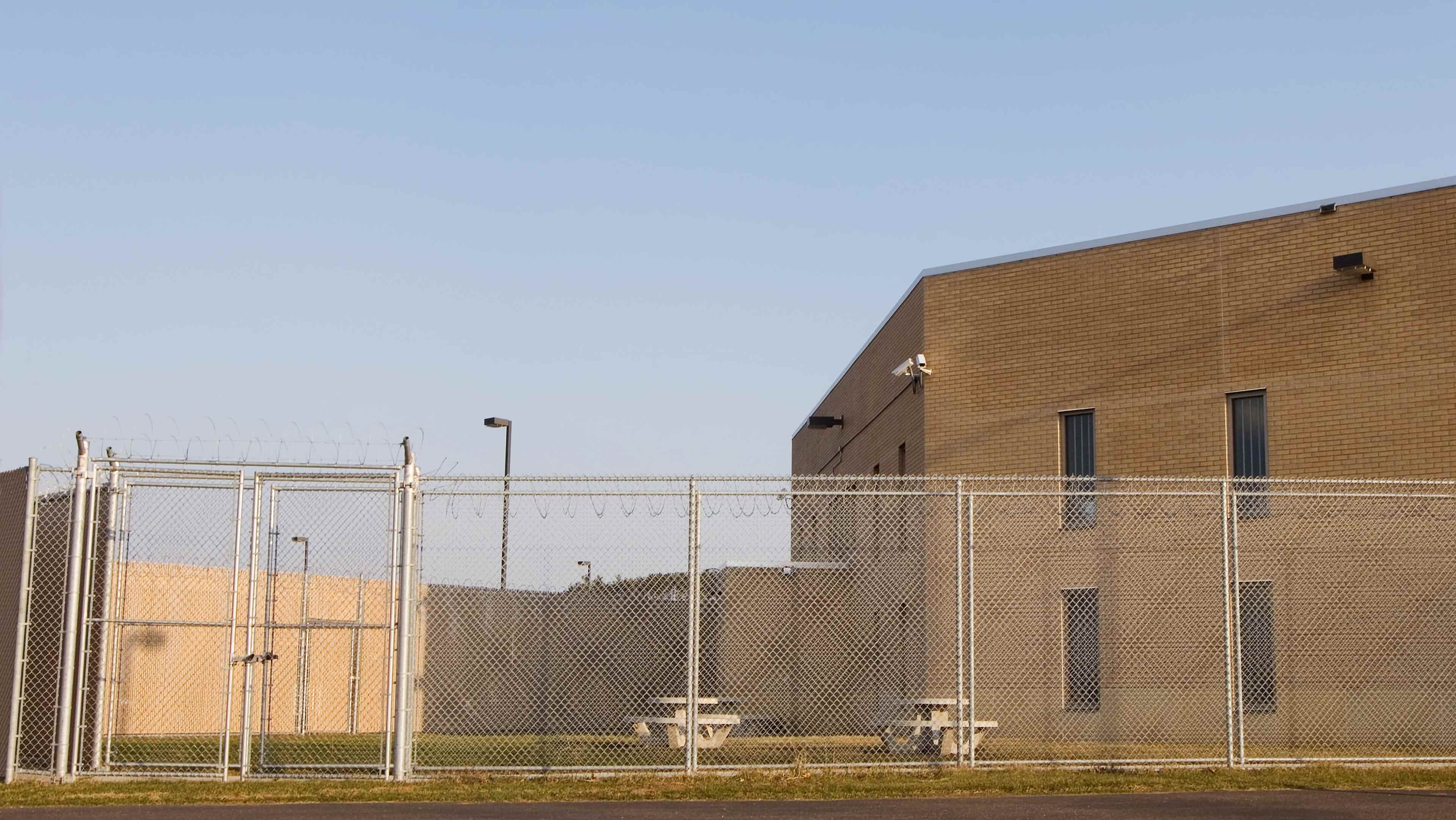 An empty fenced prison yard with prison behind