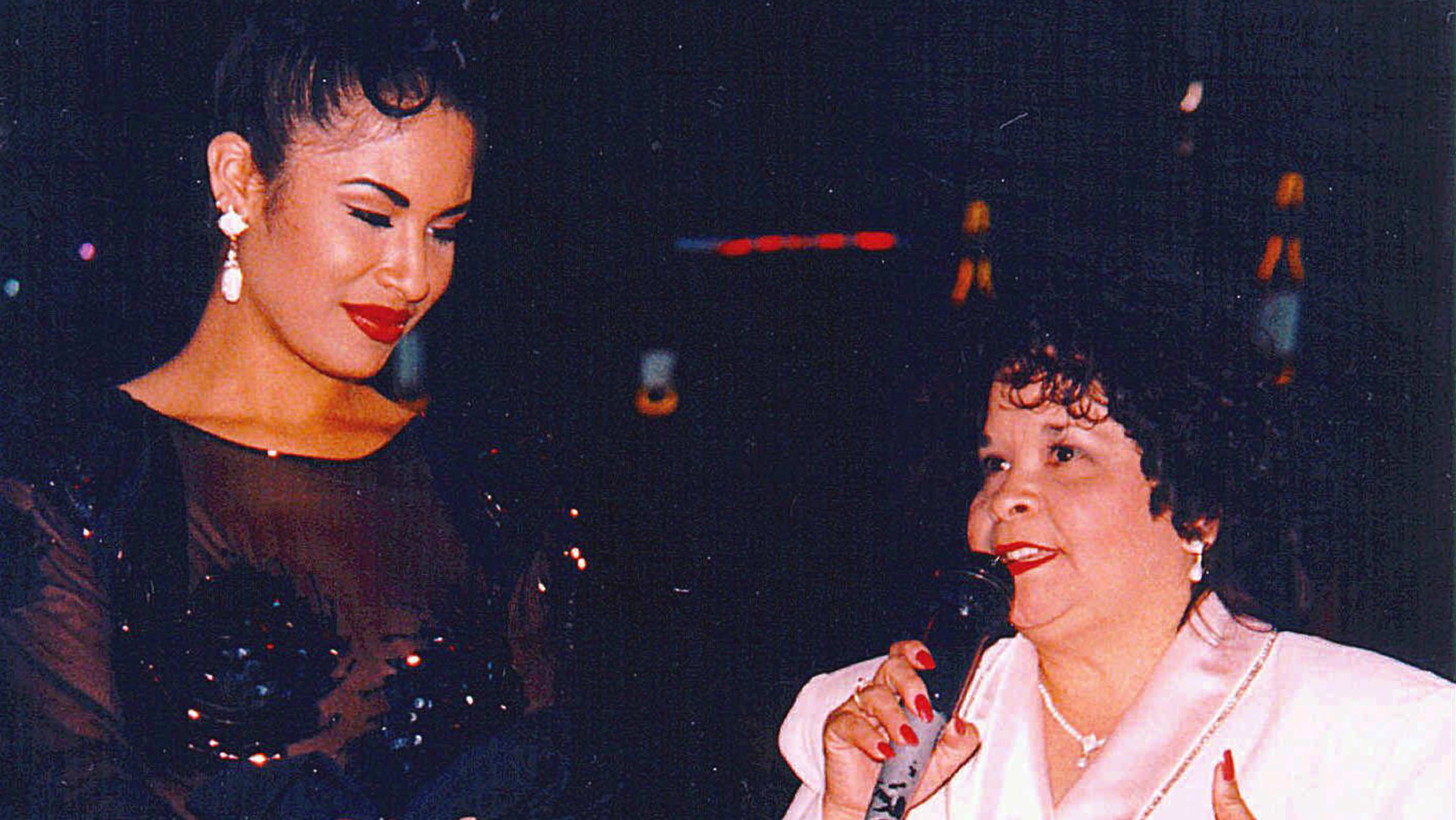 The image shows two women, one with a glamorous appearance and the other with a more casual look, engaged in conversation and appearing to be enjoying each other's company.
