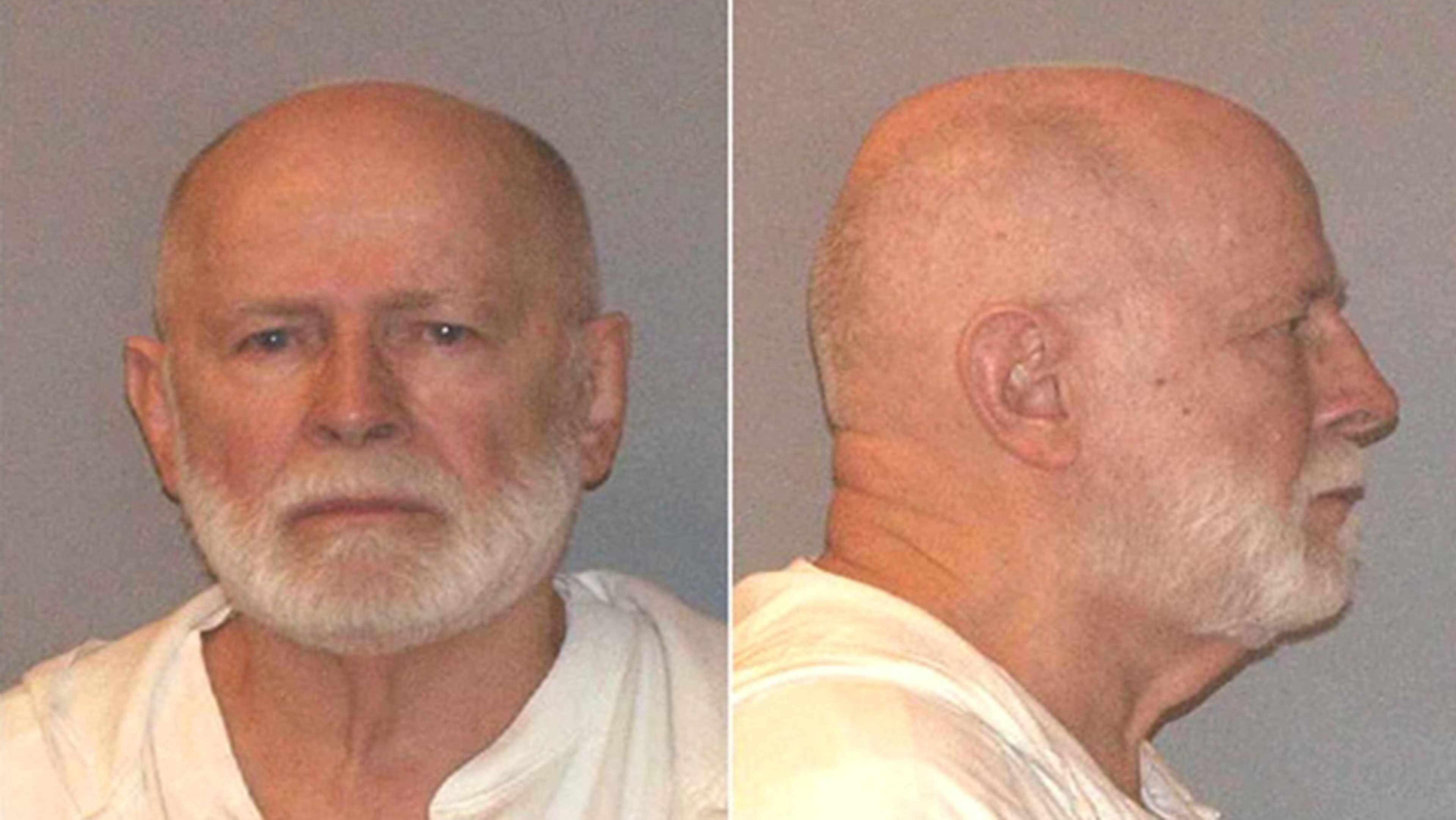 The image shows a close-up portrait of an elderly man with a long white beard, wearing a light-colored shirt, against a plain gray background.