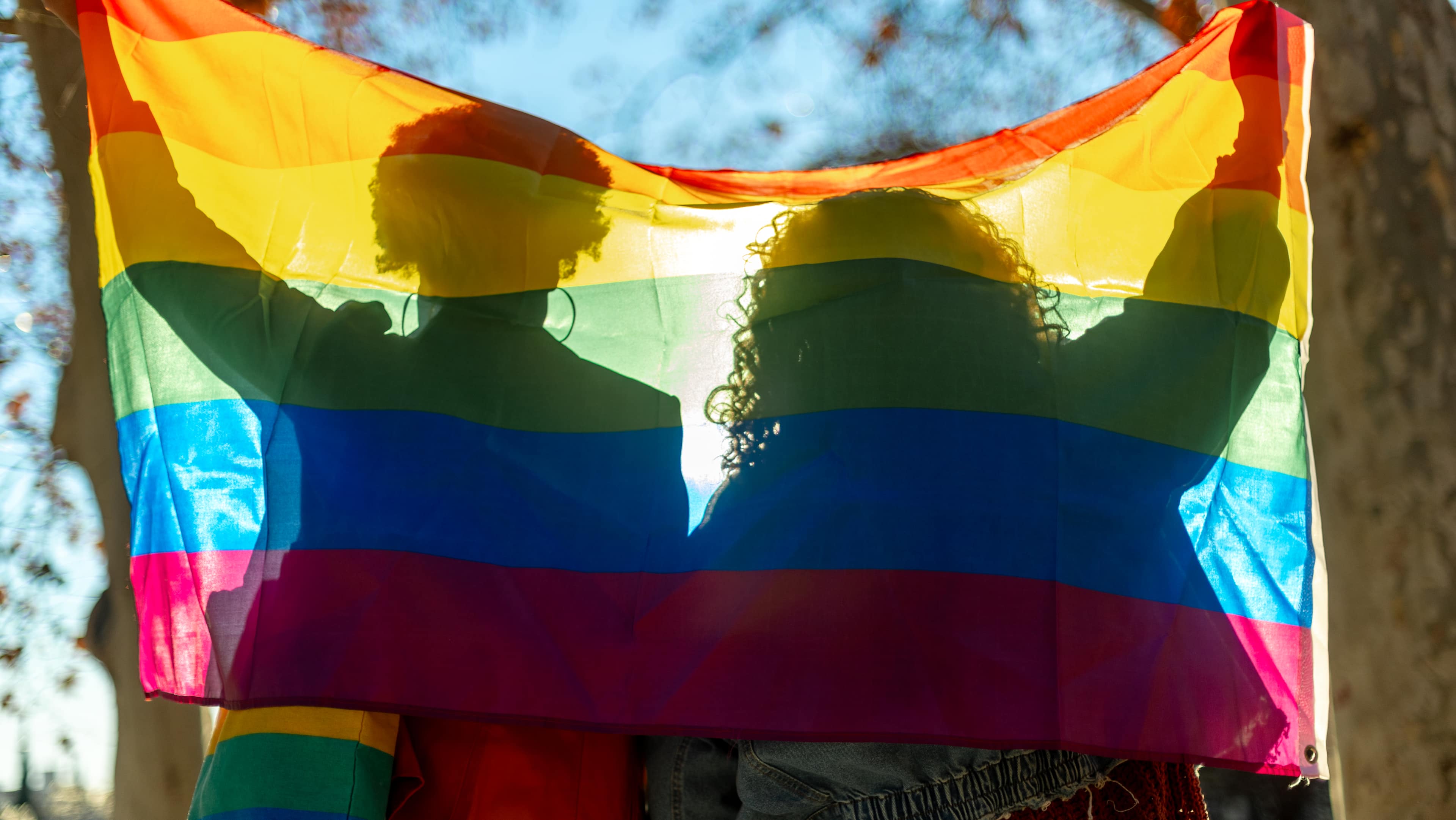 Two people holding a lgbt flag behind their backs