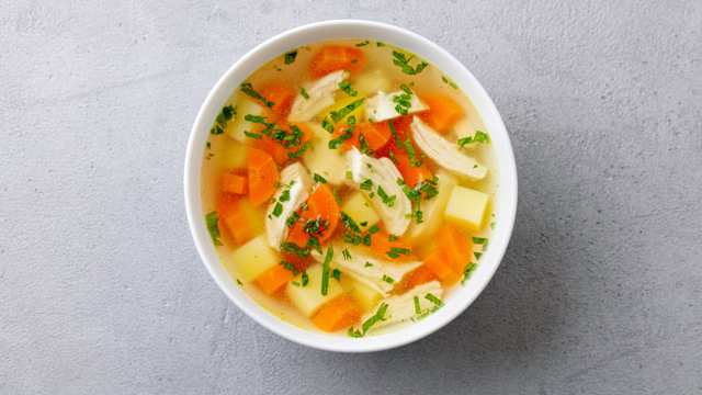 Chicken soup with vegetables in white bowl. Grey stone background. Top view.