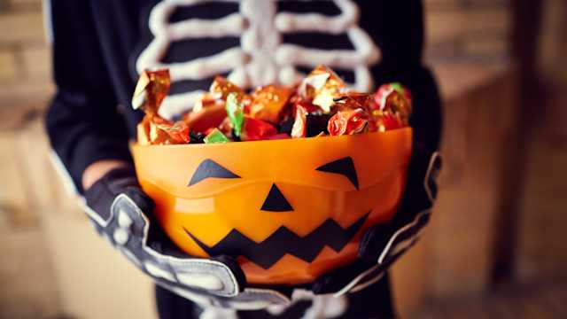 Boy in skeleton costume holding bowl full of halloween candy