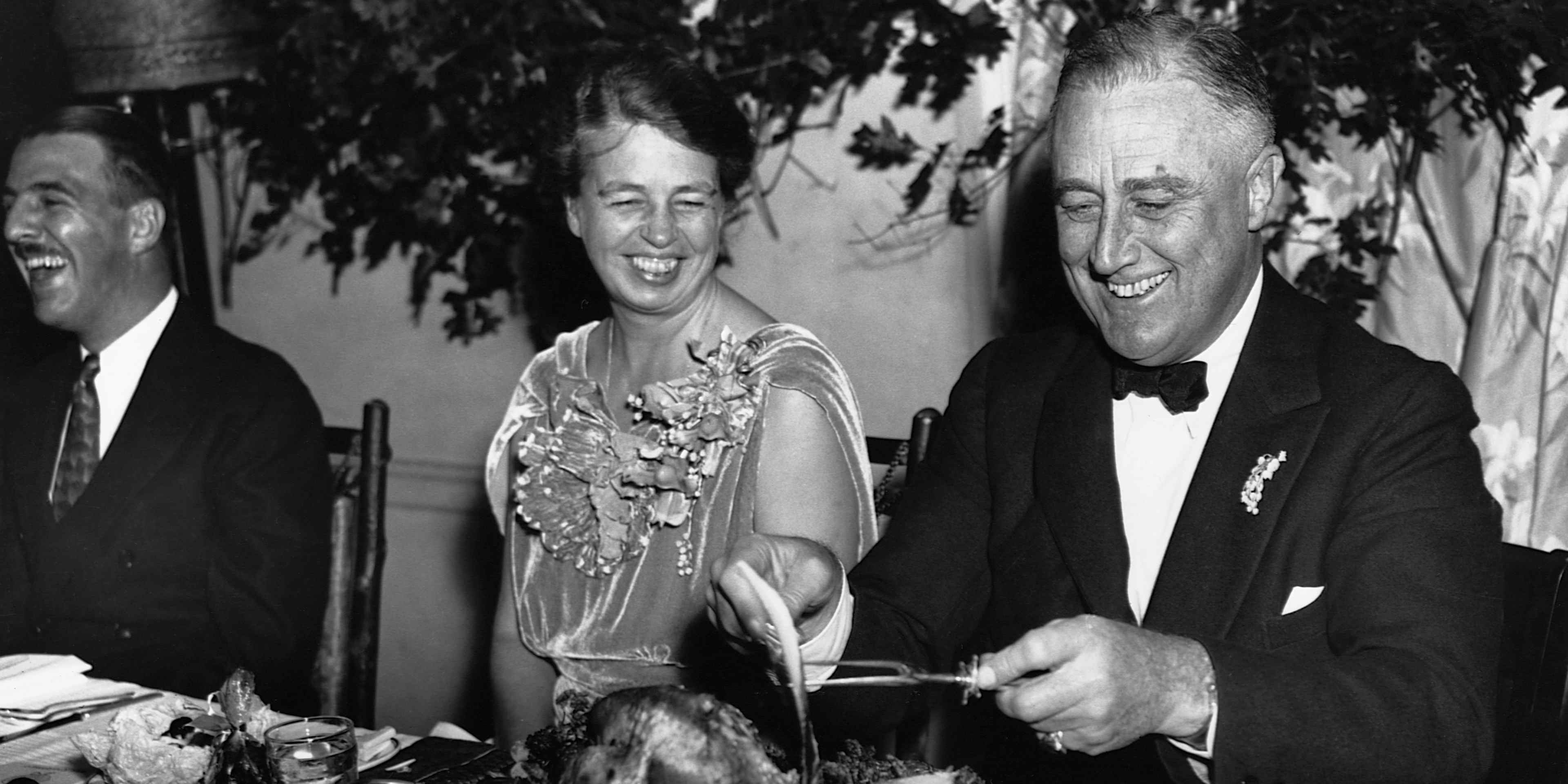 First Lady Eleanor Roosevelt and President Franklin D. Roosevelt smile while sitting at a table as Franklin slices a turkey