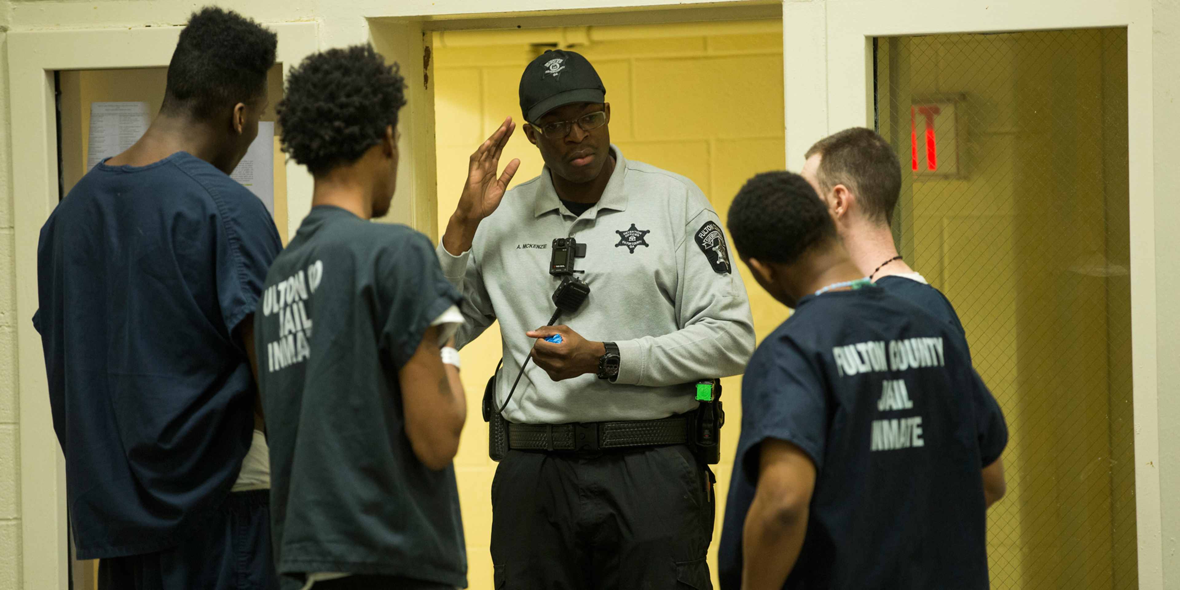 A group of individuals, some wearing uniforms, appear to be engaged in a conversation or interaction in what seems to be a hallway or corridor setting.