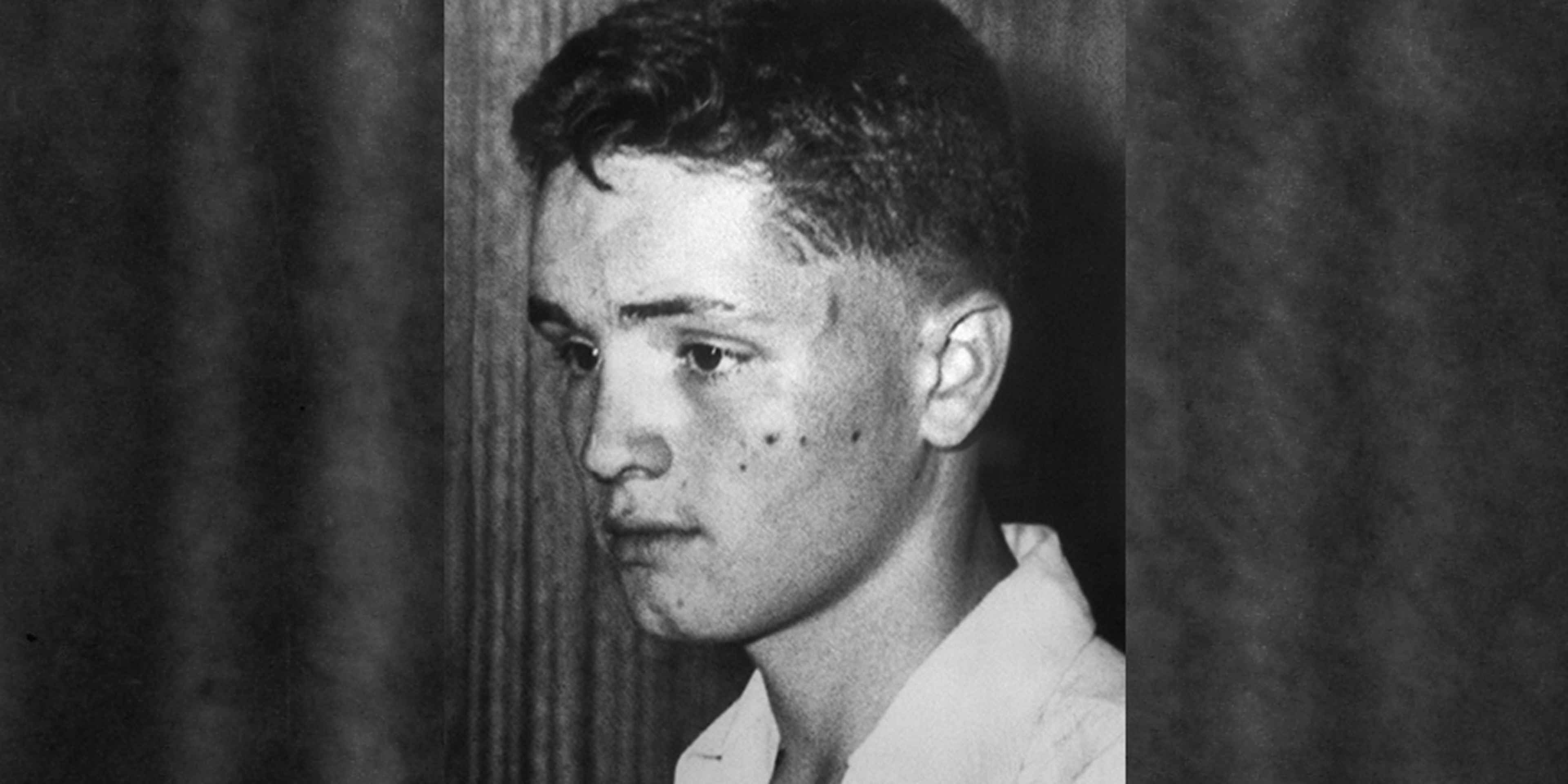 A black and white portrait of a young man with a serious expression, set against a dark background.