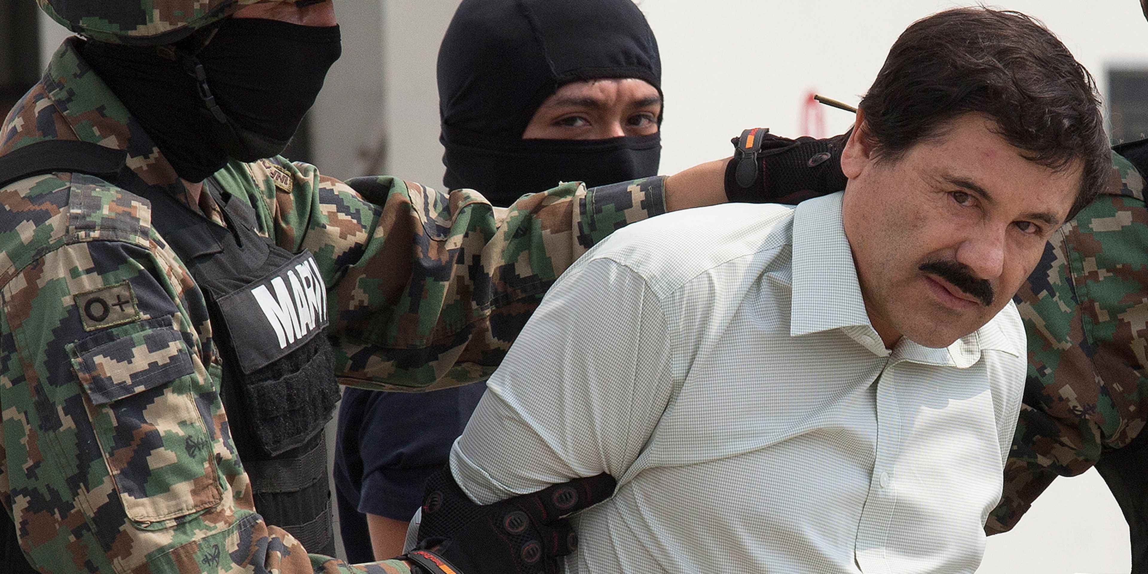 The image shows a man in a white shirt being escorted by two individuals wearing camouflage and black masks, suggesting a law enforcement or military context.