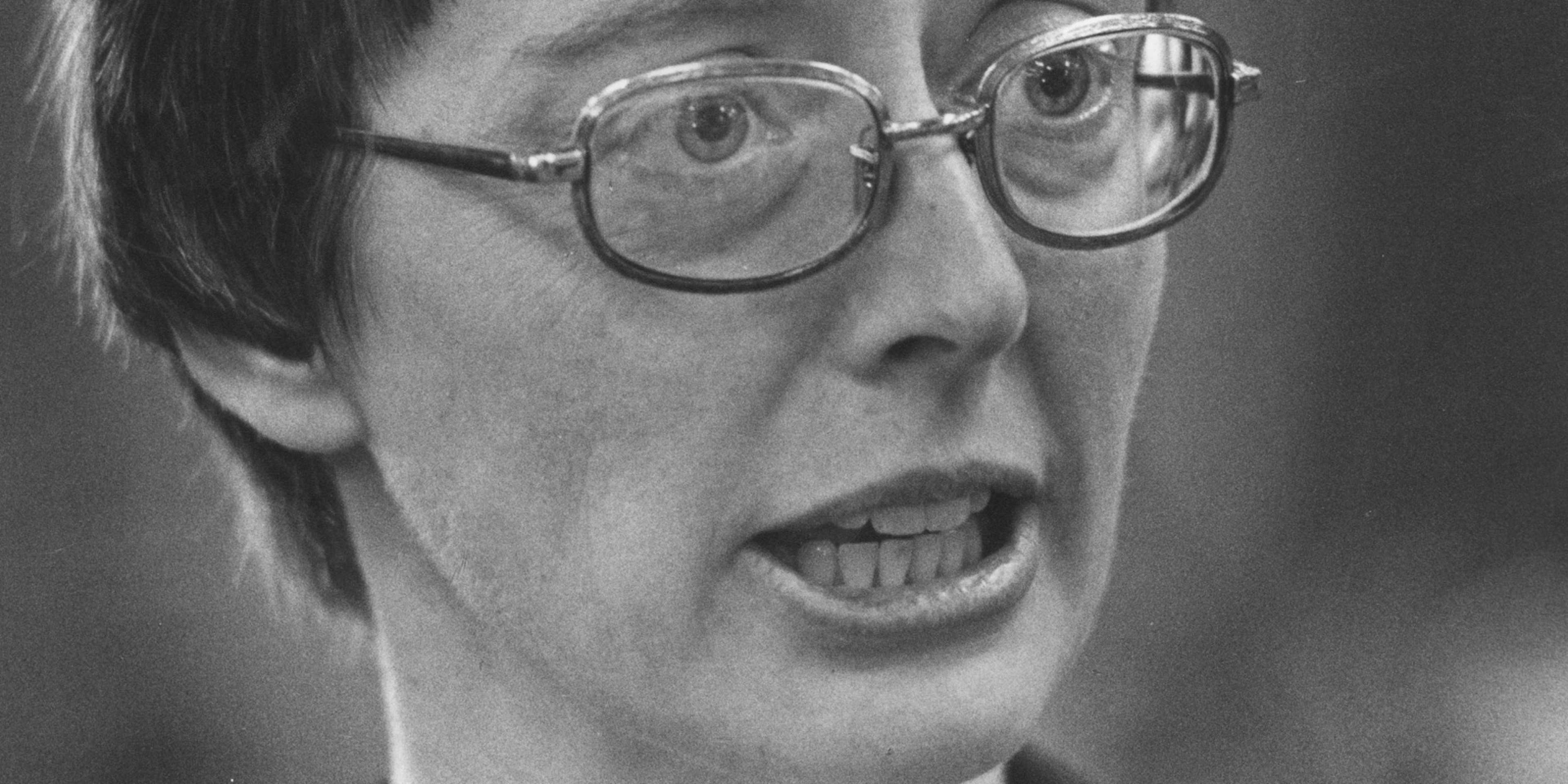 A close-up black and white portrait of a person with glasses, their mouth open in an expression of surprise or excitement.