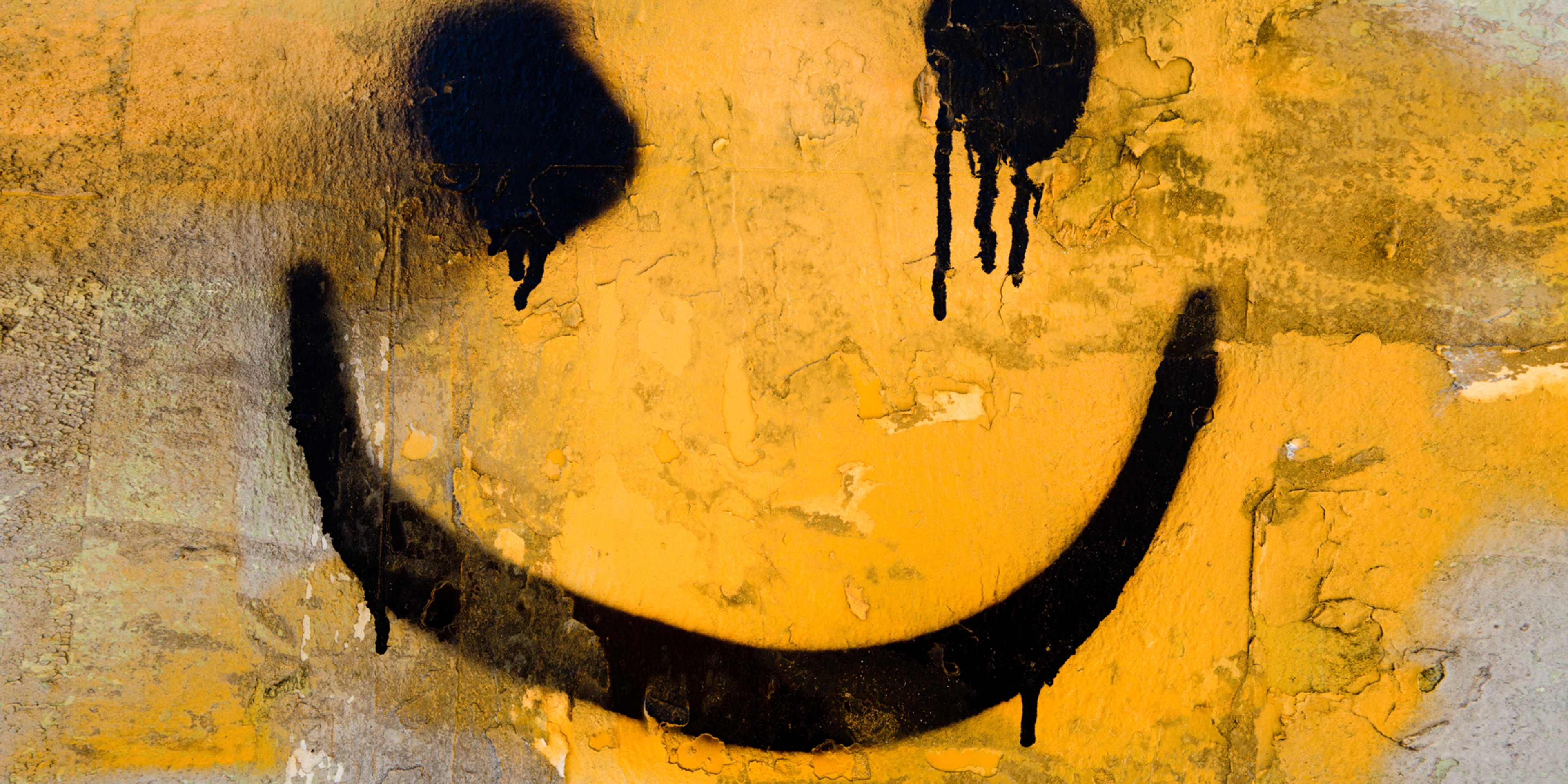 A large, stylized smiley face with dripping black paint or ink against a textured, golden-yellow background.