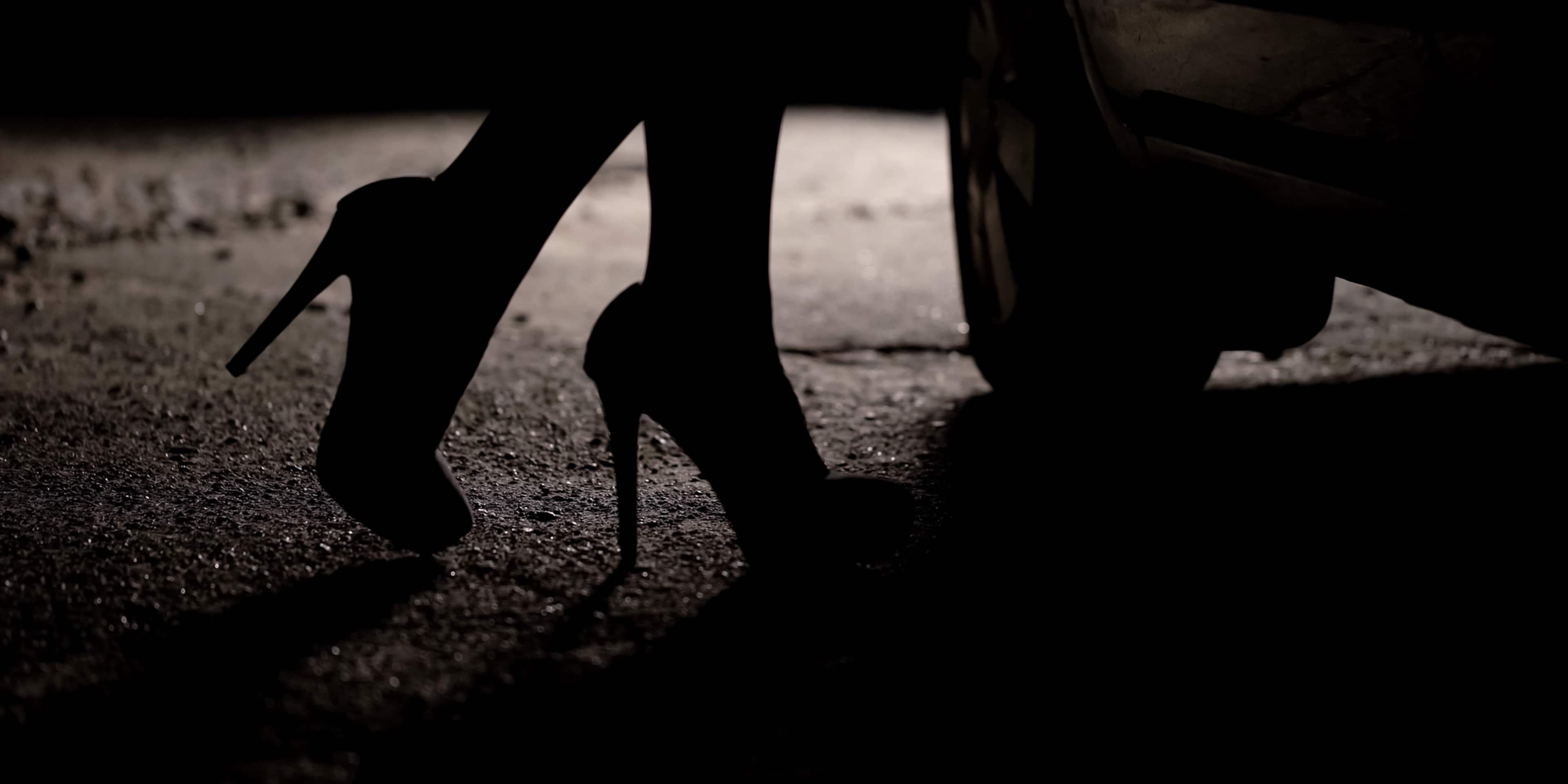 A silhouetted figure stands on a gravel path, with a dark, shadowy background.