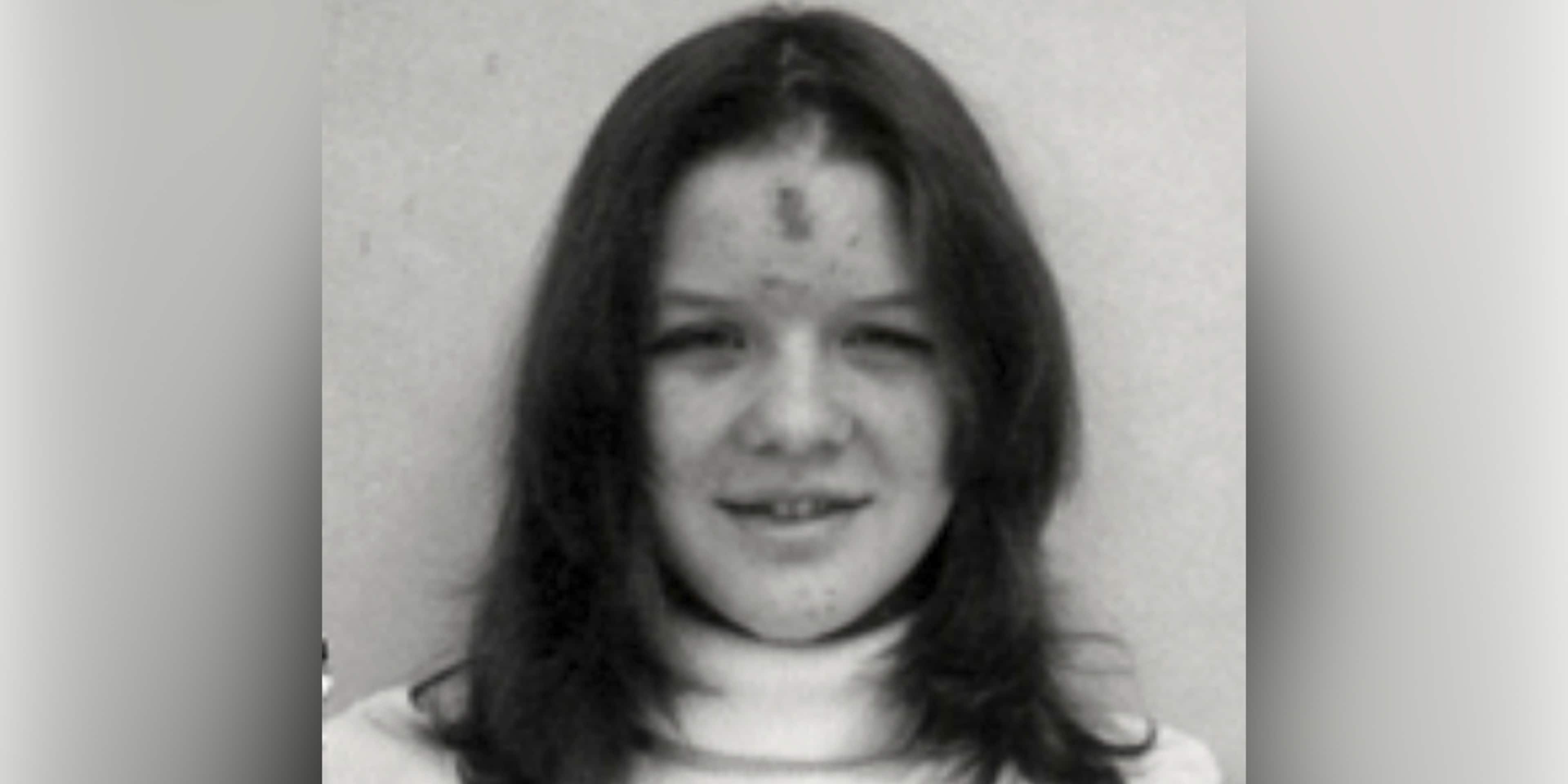 A black and white portrait photograph of a young woman with long dark hair, smiling directly at the camera.