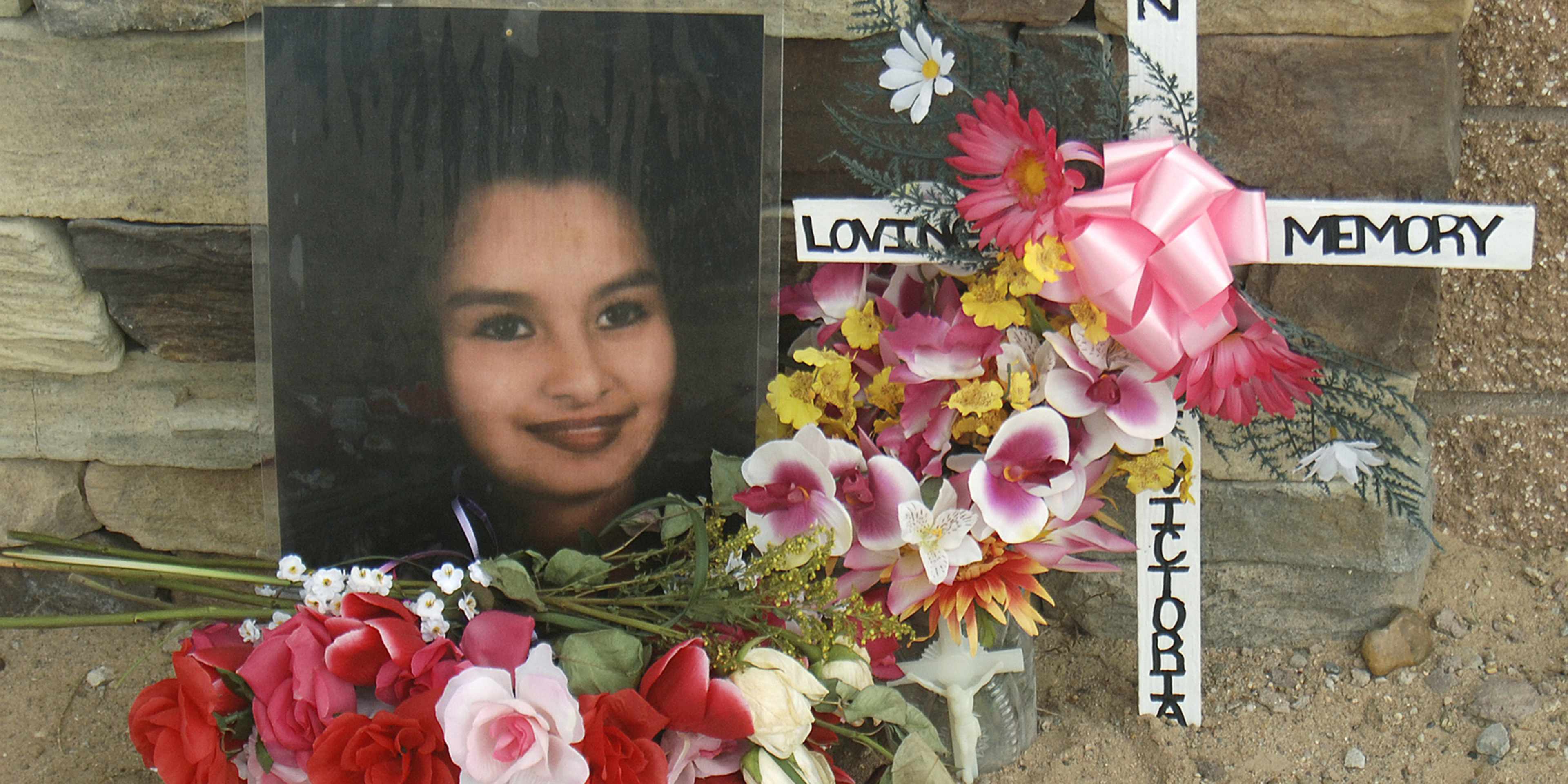 The image shows a memorial display with a framed photograph of a person, surrounded by various colorful flowers and decorations, including the words "Loving Memory" and "In Loving Memory" written on signs.