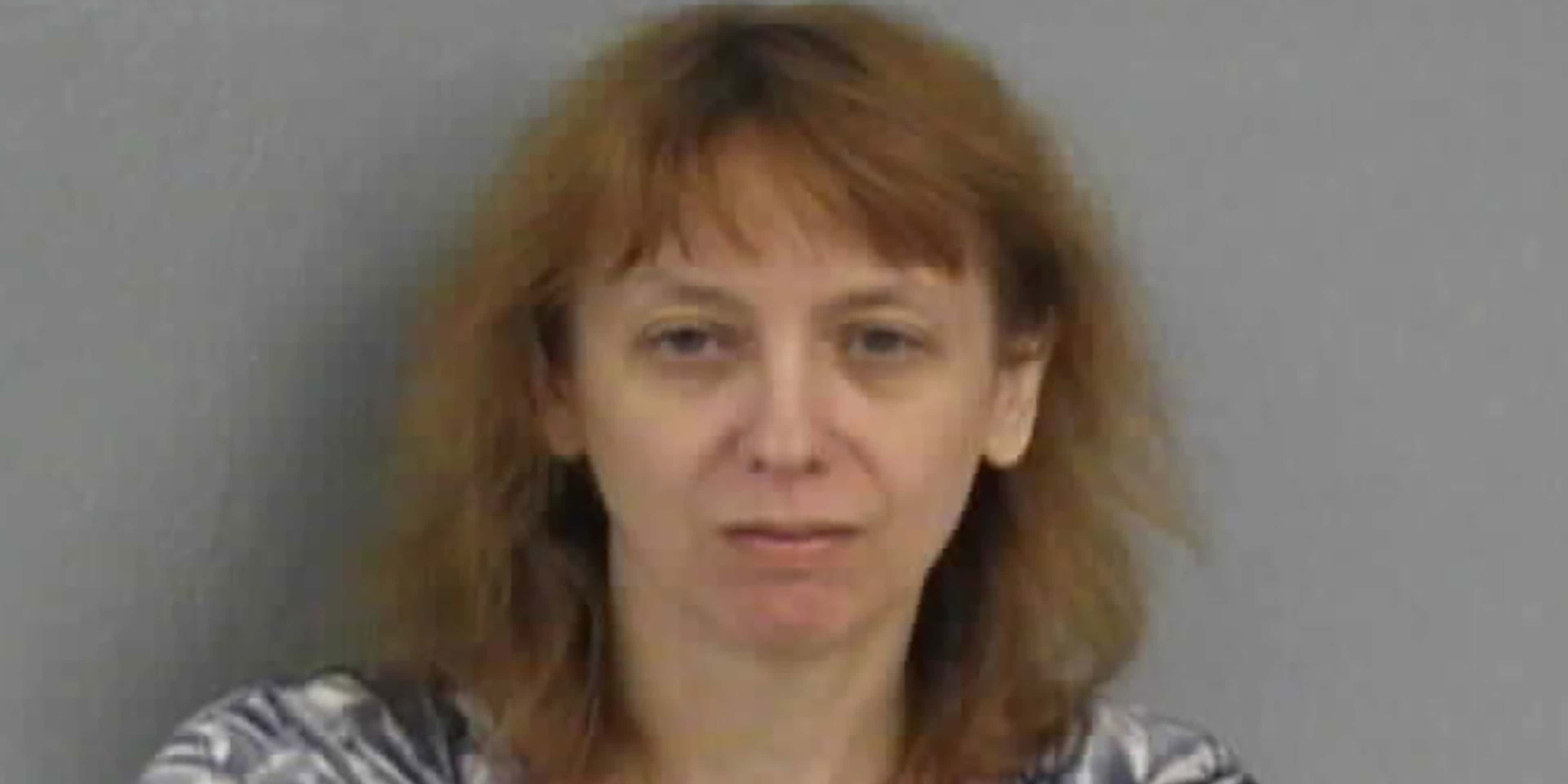 The image shows a middle-aged woman with shoulder-length brown hair, wearing a striped shirt, and appearing to be in a neutral expression against a plain gray background.