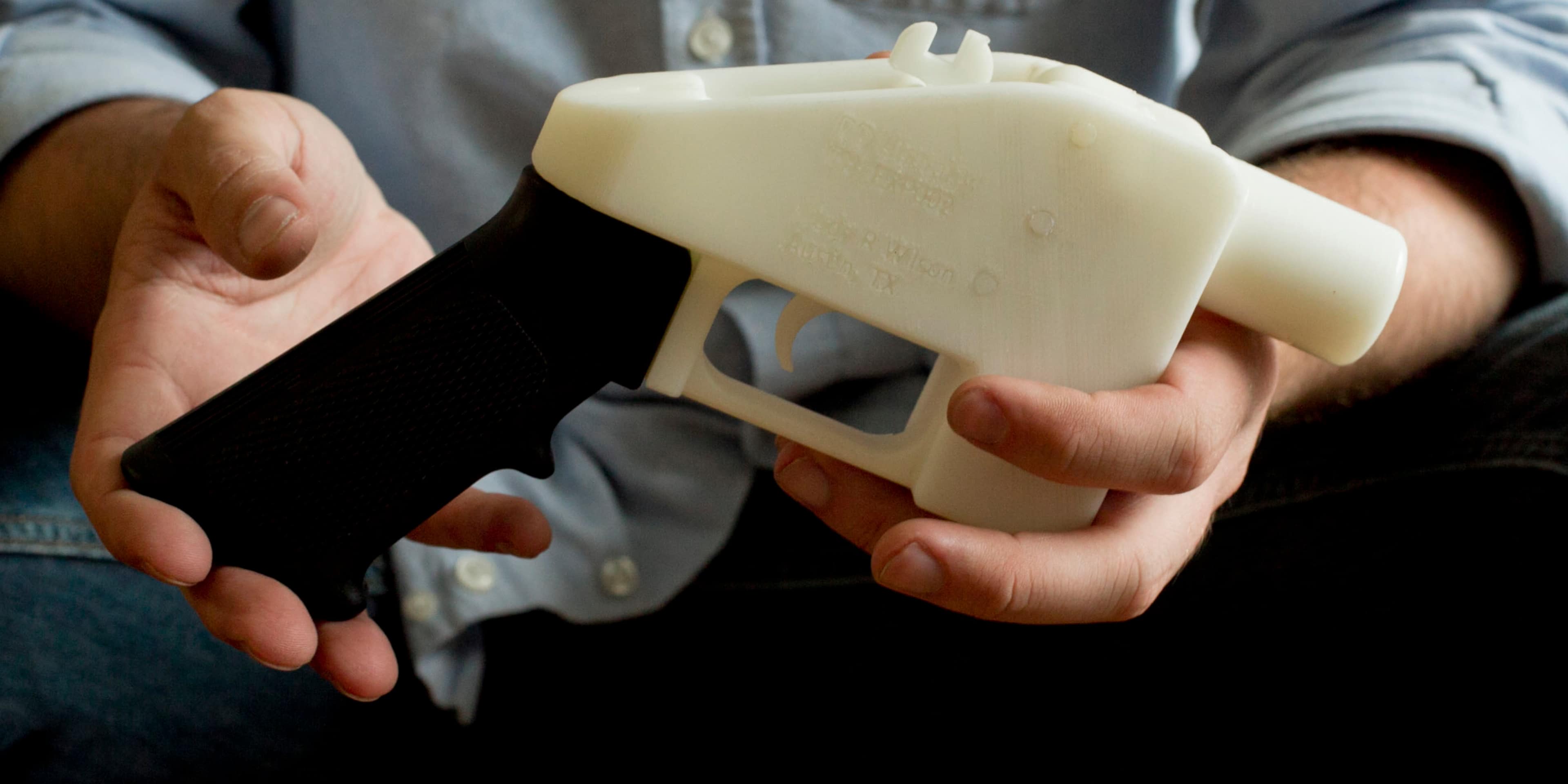 A person's hands are holding a 3D-printed plastic gun-shaped object against a blurred background.
