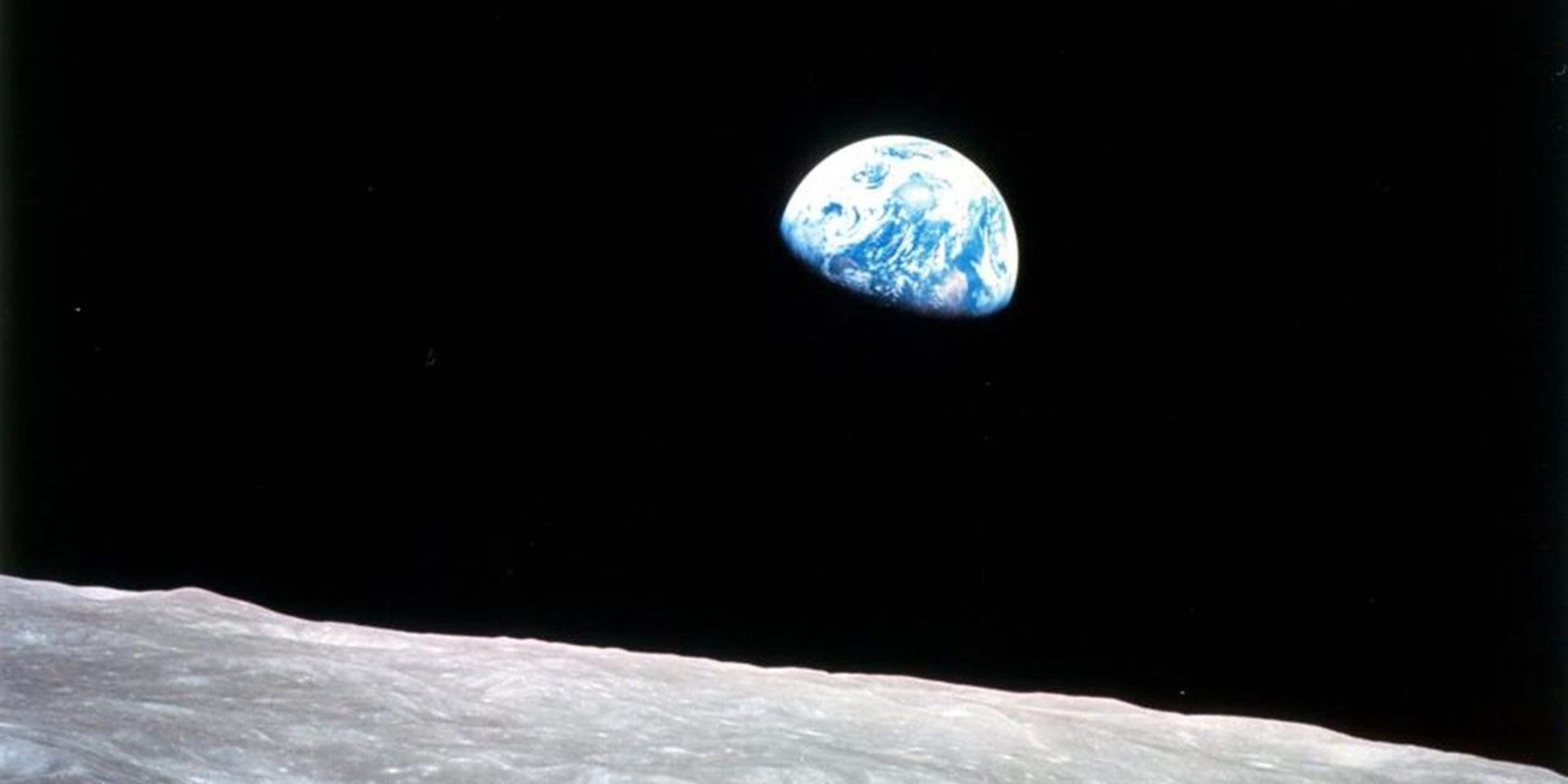 Blue-and-white orb of the earth in the vast blackness of space hanging over the crater-pocked surface of the moon
