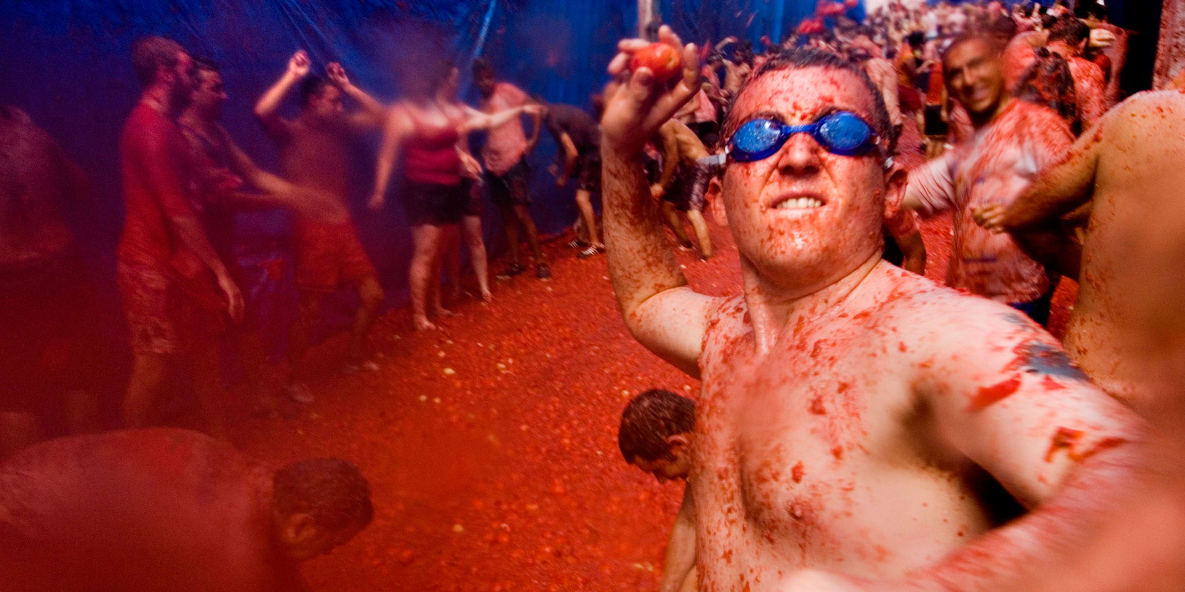 Man wearing swimming goggles throwing a tomato at La tomatina food fighting festival. Bunol. Valencia Spain