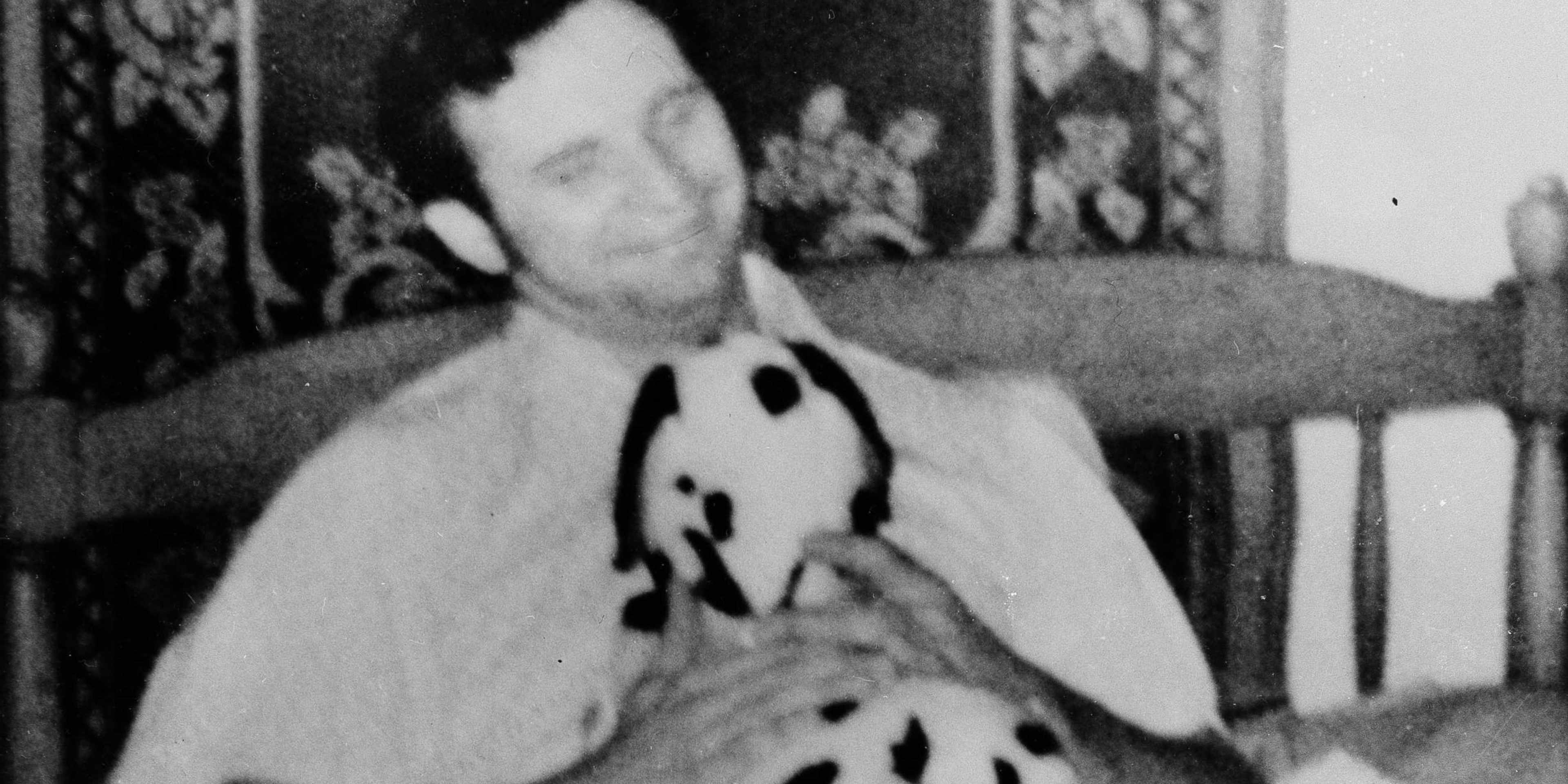 A person wearing a polka dot outfit is sitting in a chair against a patterned background.