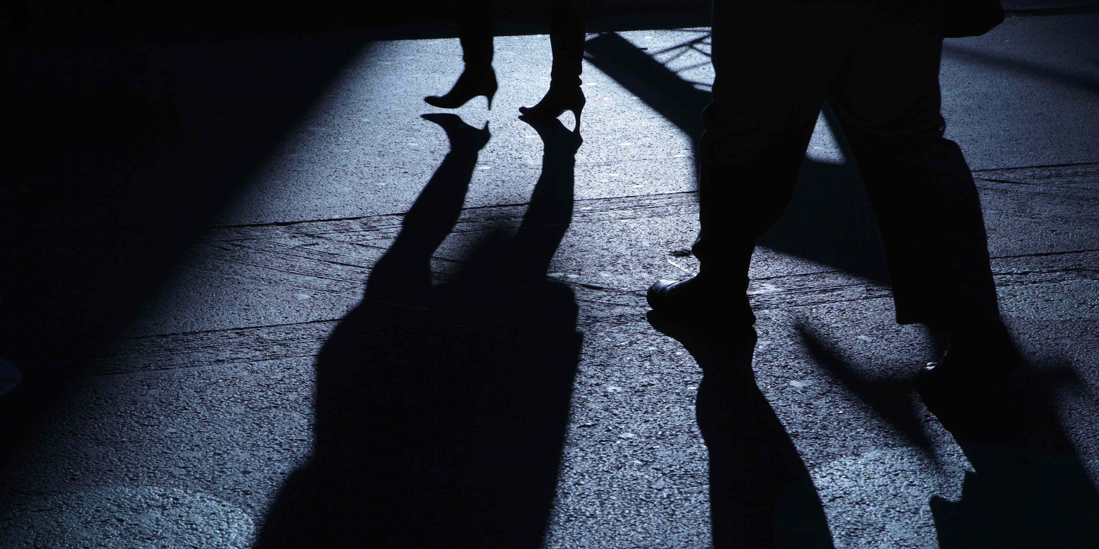 The image depicts the silhouettes of two people walking on a dimly lit street, their shadows cast on the ground creating an intriguing and mysterious atmosphere.