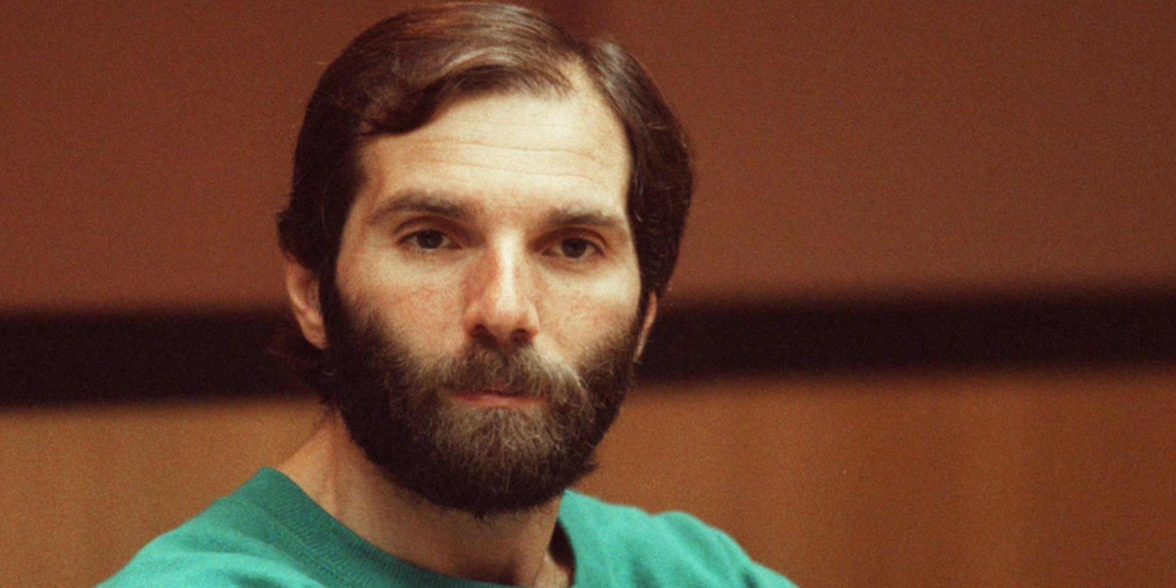 A man with a beard wearing a green shirt is the focus of the image, which appears to be taken in a dimly lit room.
