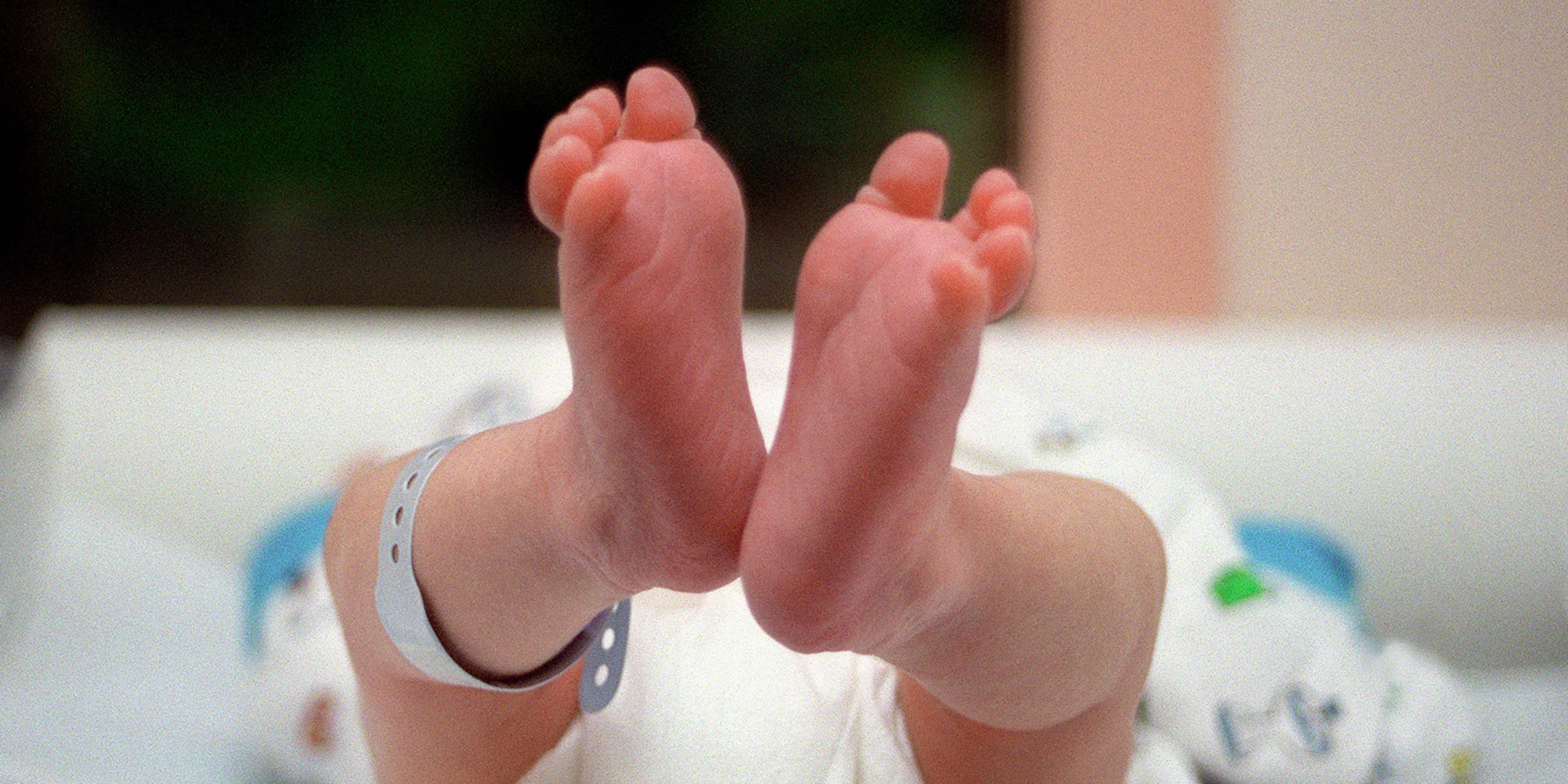 The image shows a pair of bare feet resting on a white surface, with a colorful patterned background visible behind them.