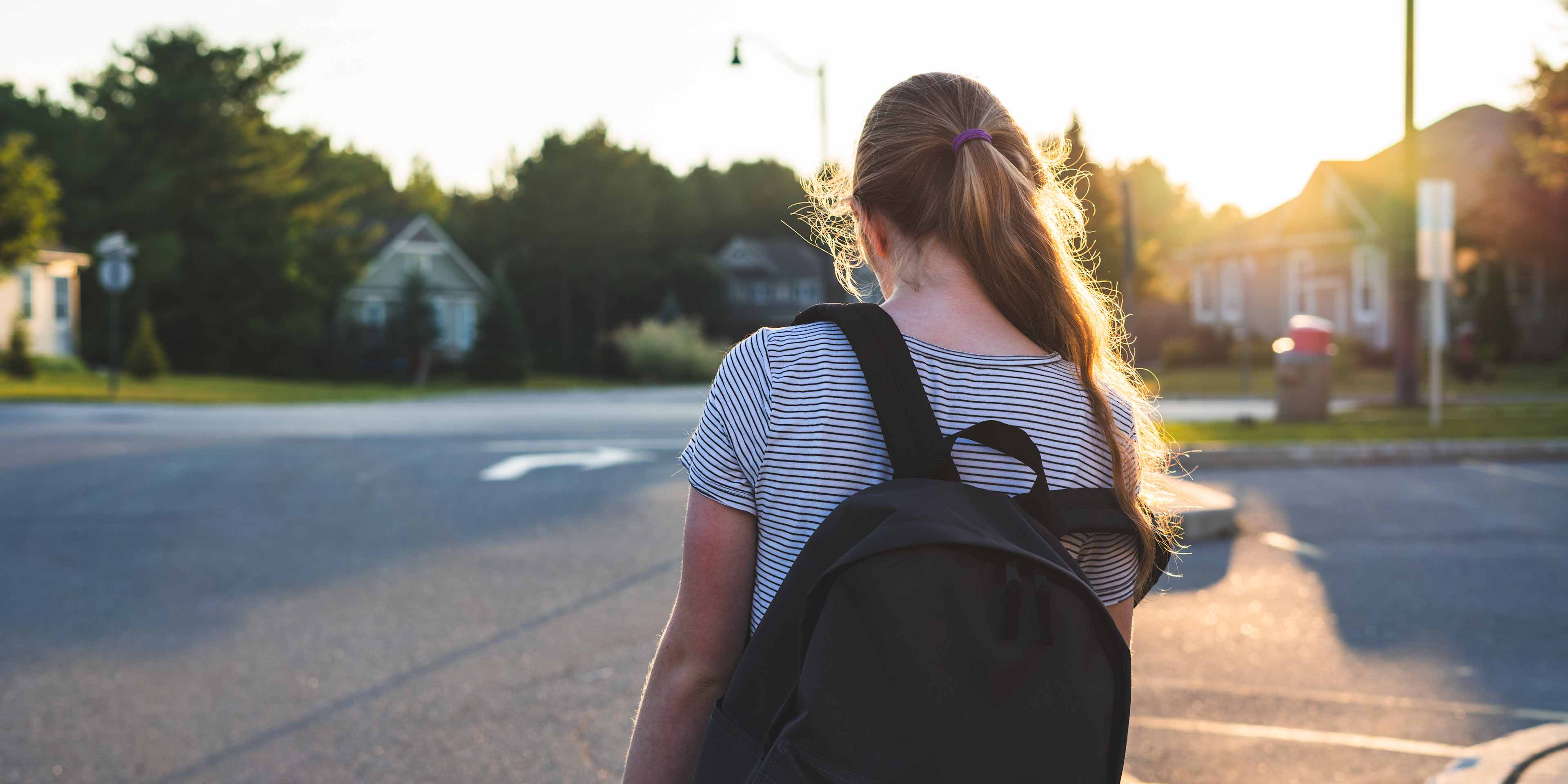 Profile of a teen girl depressed/sad at sunset in a parking lot while wearing a backpack.