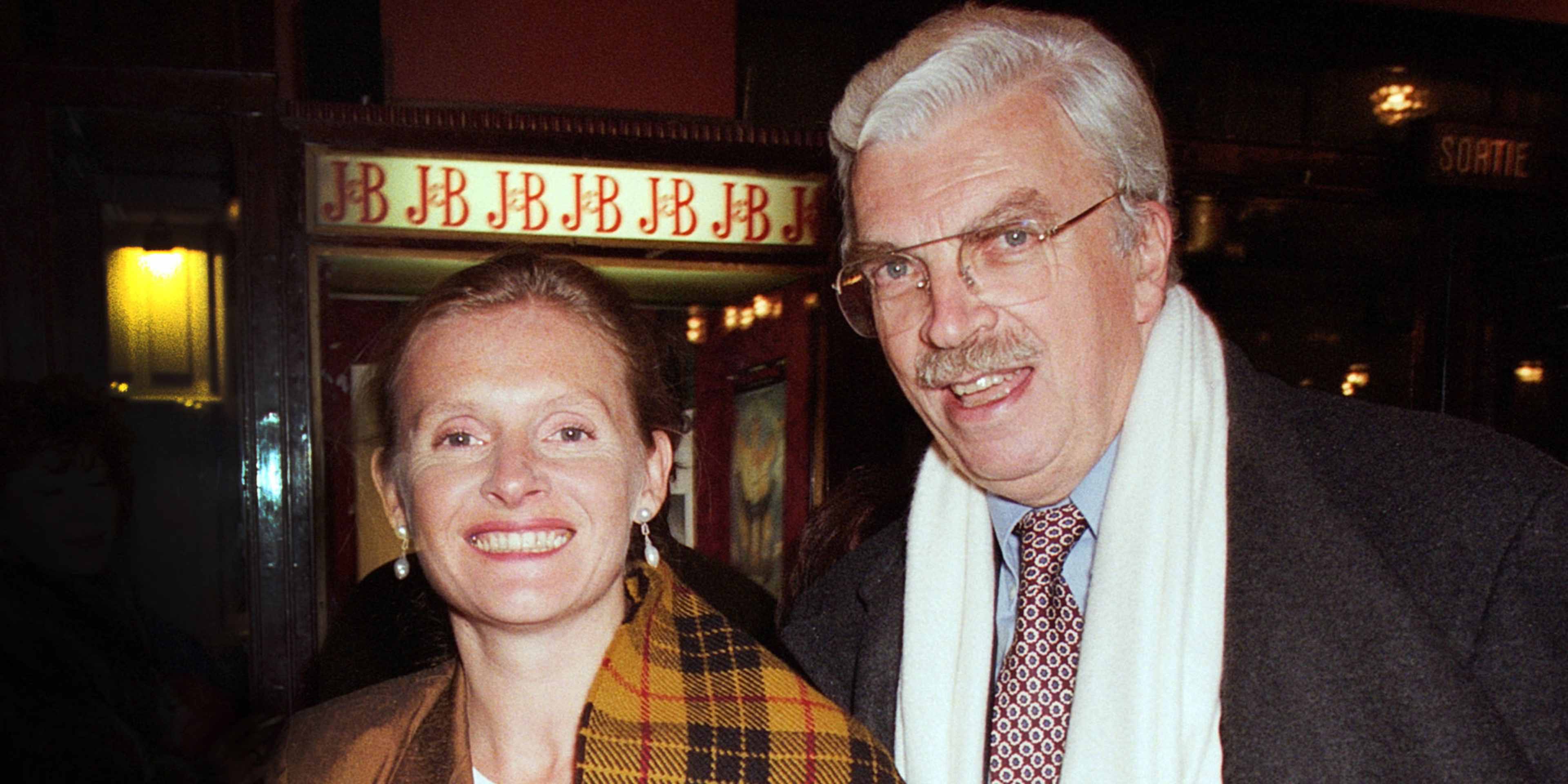 The image shows an older couple, a man and a woman, standing together and smiling in front of a theater marquee with the word "BBBBB" displayed.
