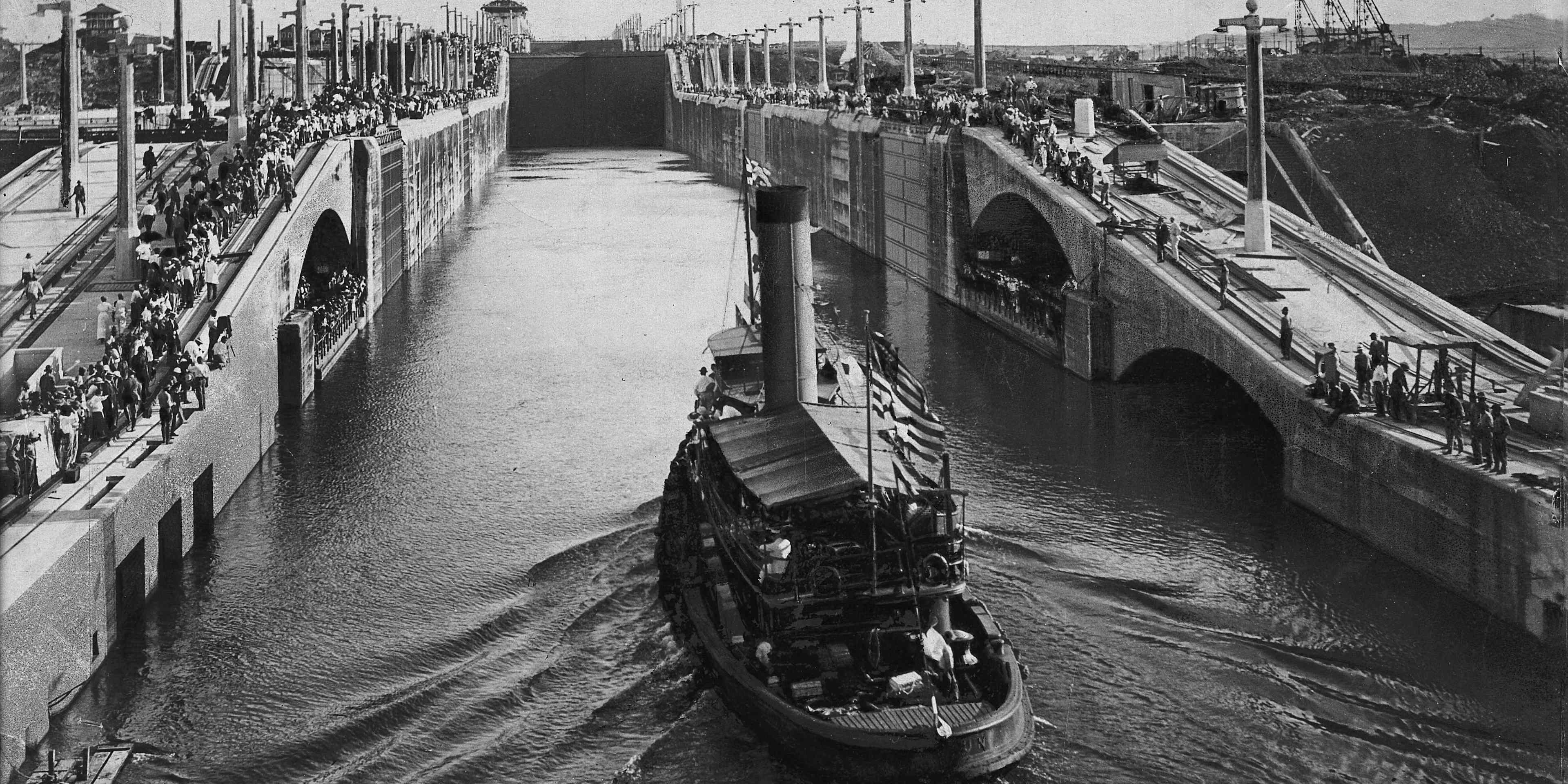 black and white photo of a boat in the Panama Canal, with spectators on either side of the waterway