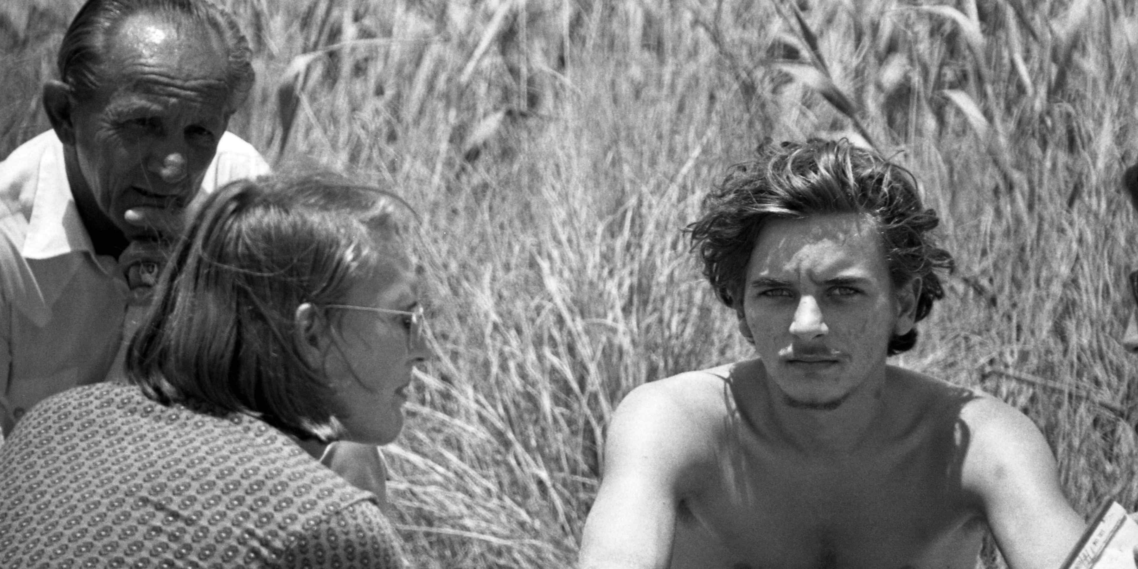 The image depicts two people, a man and a woman, standing in a field of tall grass.