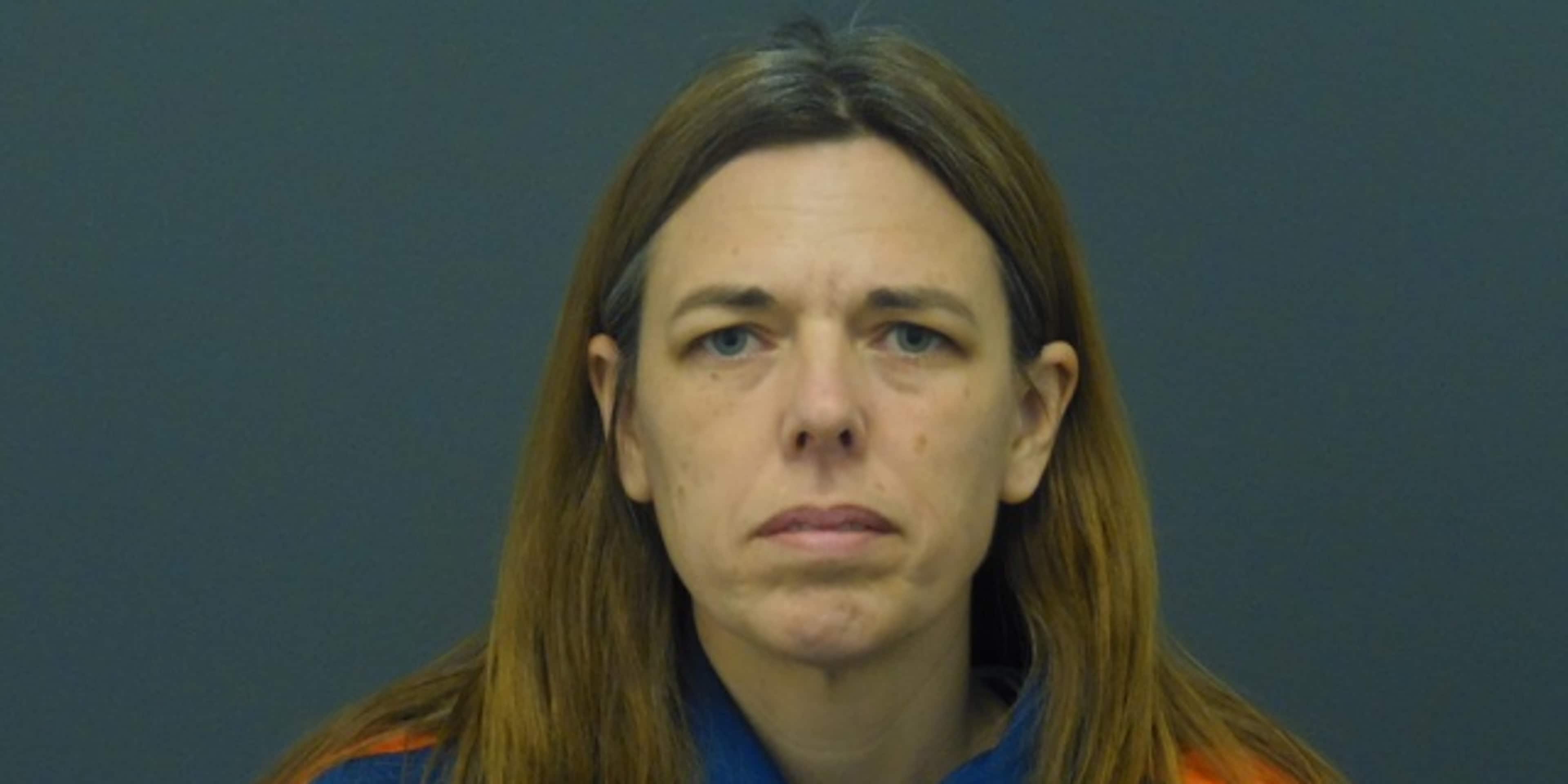 A woman with long brown hair wearing a blue and orange uniform stands against a dark background.
