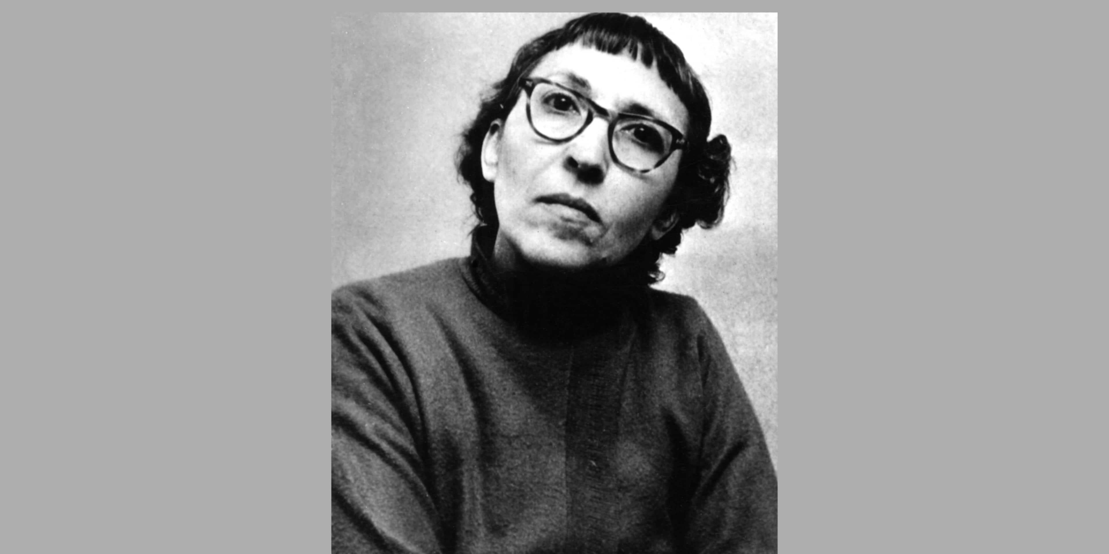 A black and white portrait of a person wearing glasses and a turtleneck sweater, with a serious expression on their face.