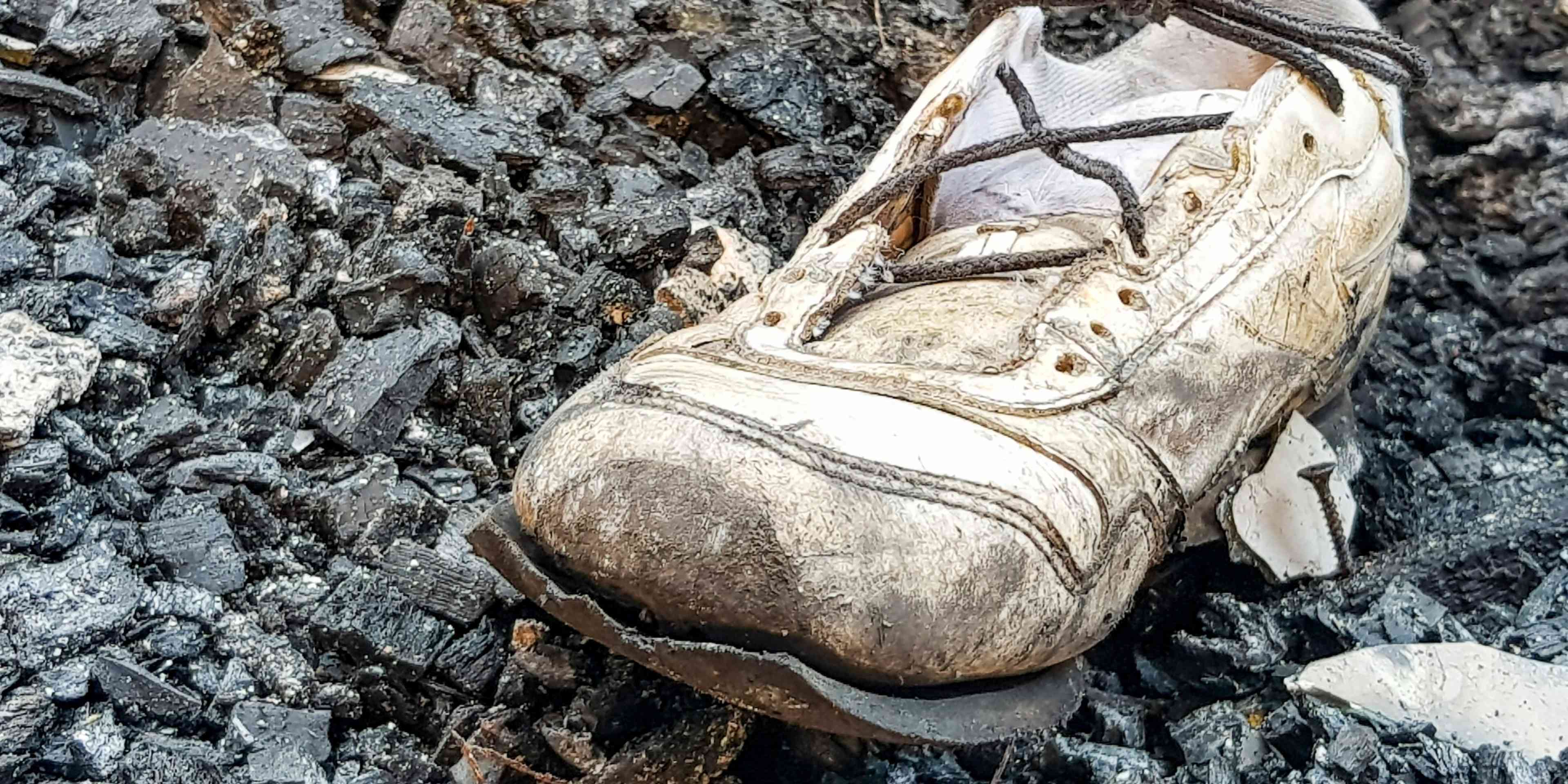 A worn, weathered hiking boot rests on a rocky, snow-covered surface.