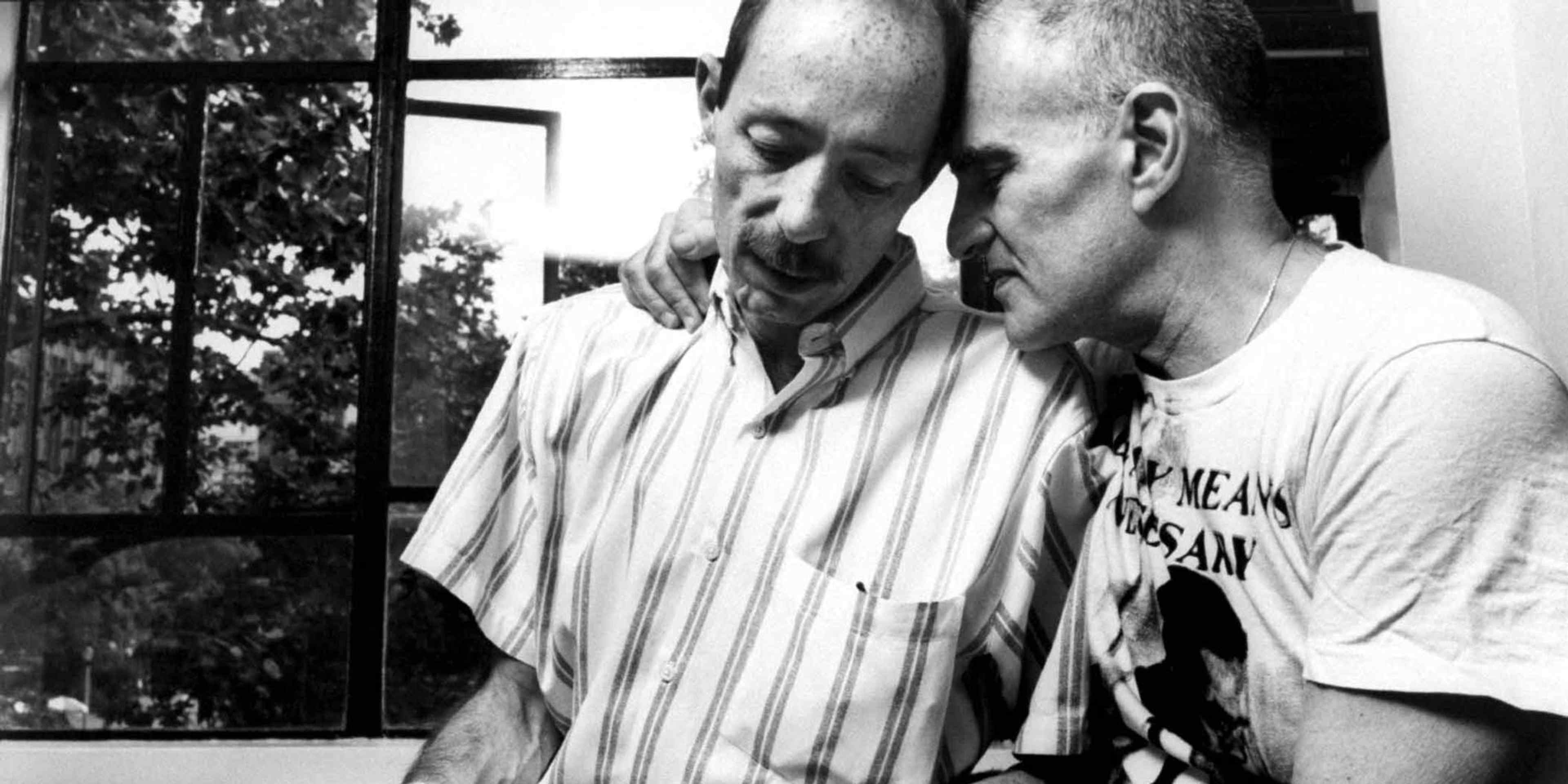 Author/gay activist Larry Kramer, founder of ACT UP, snuggling w. his friend, author & AIDS victim Vito Russo, as he tries to comfort him while petting his dog at home