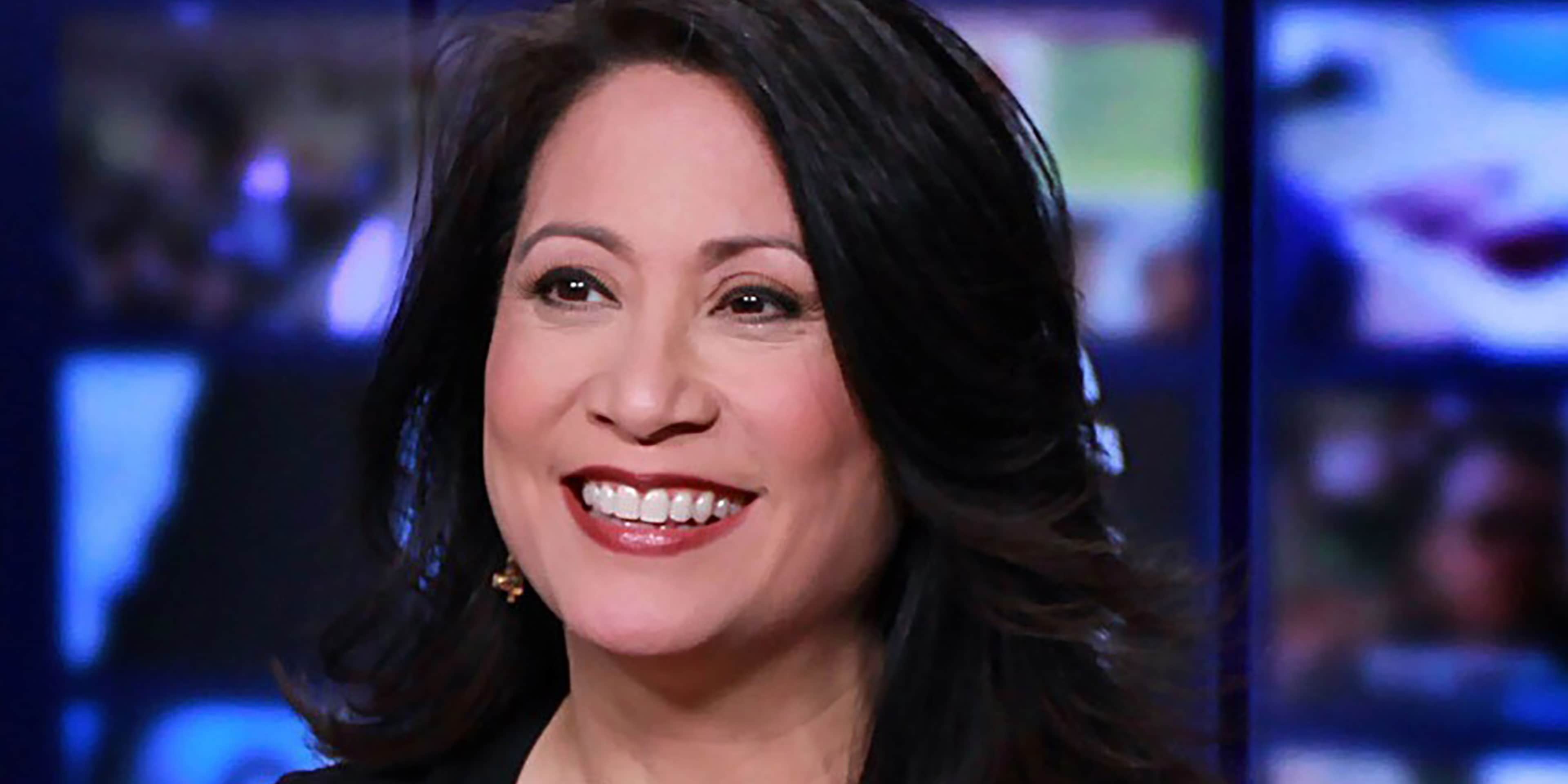The image shows a smiling woman with dark hair against a blurred blue background.