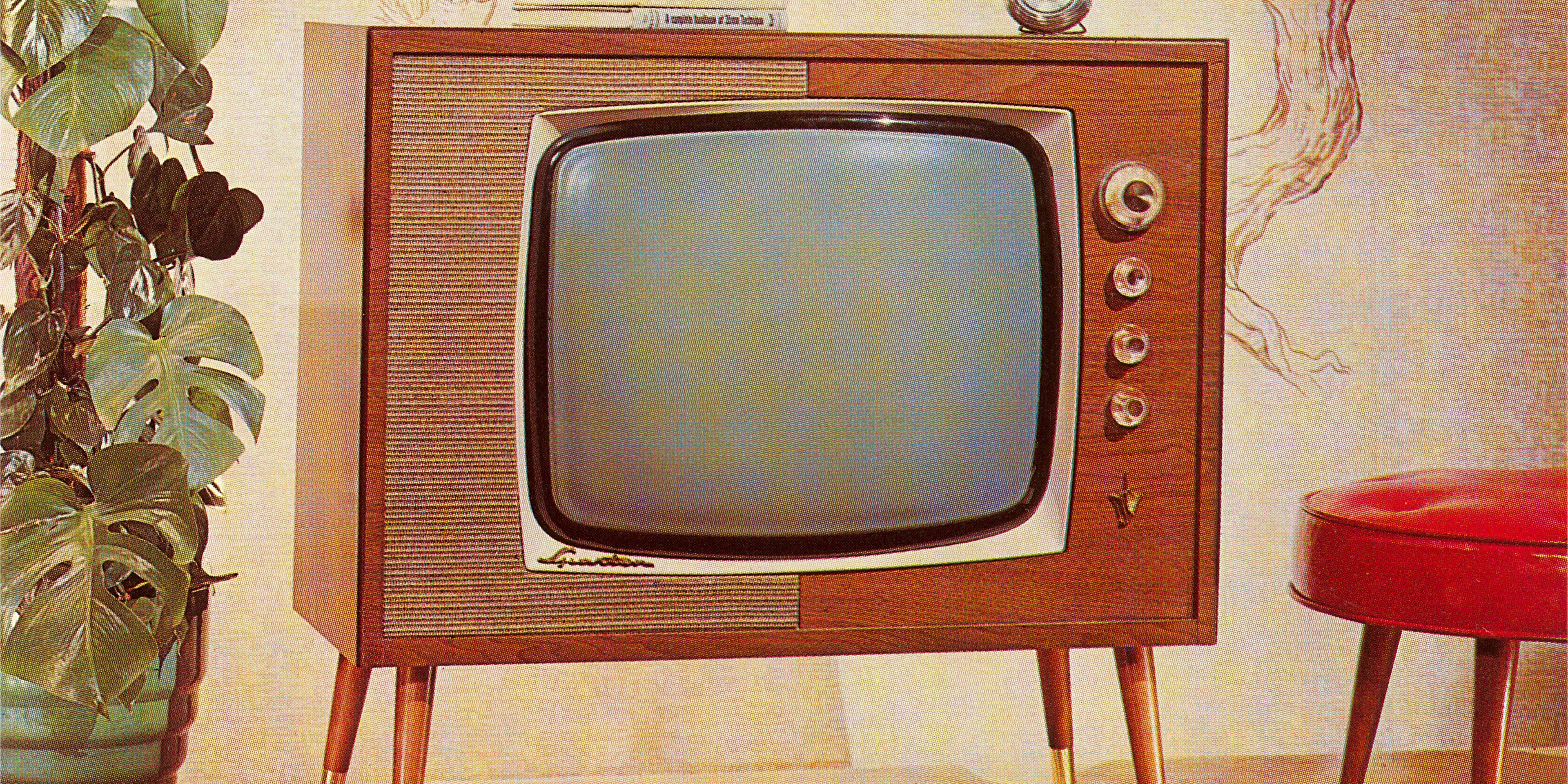 A 1960s-era TV set on legs is shown between a potted plant and red footstool.