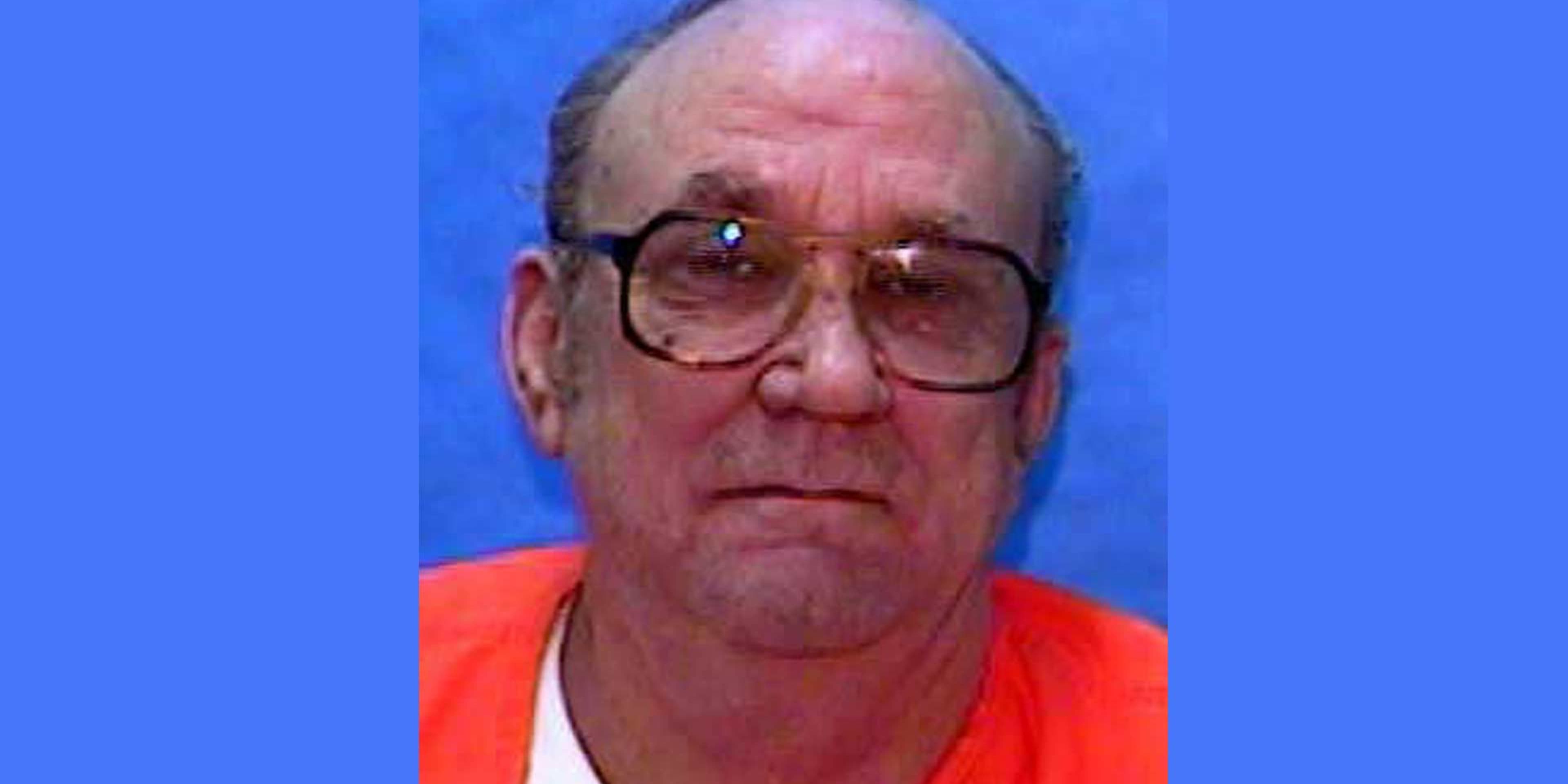 The image shows an elderly man with gray hair and glasses, wearing a red shirt, against a blue background.
