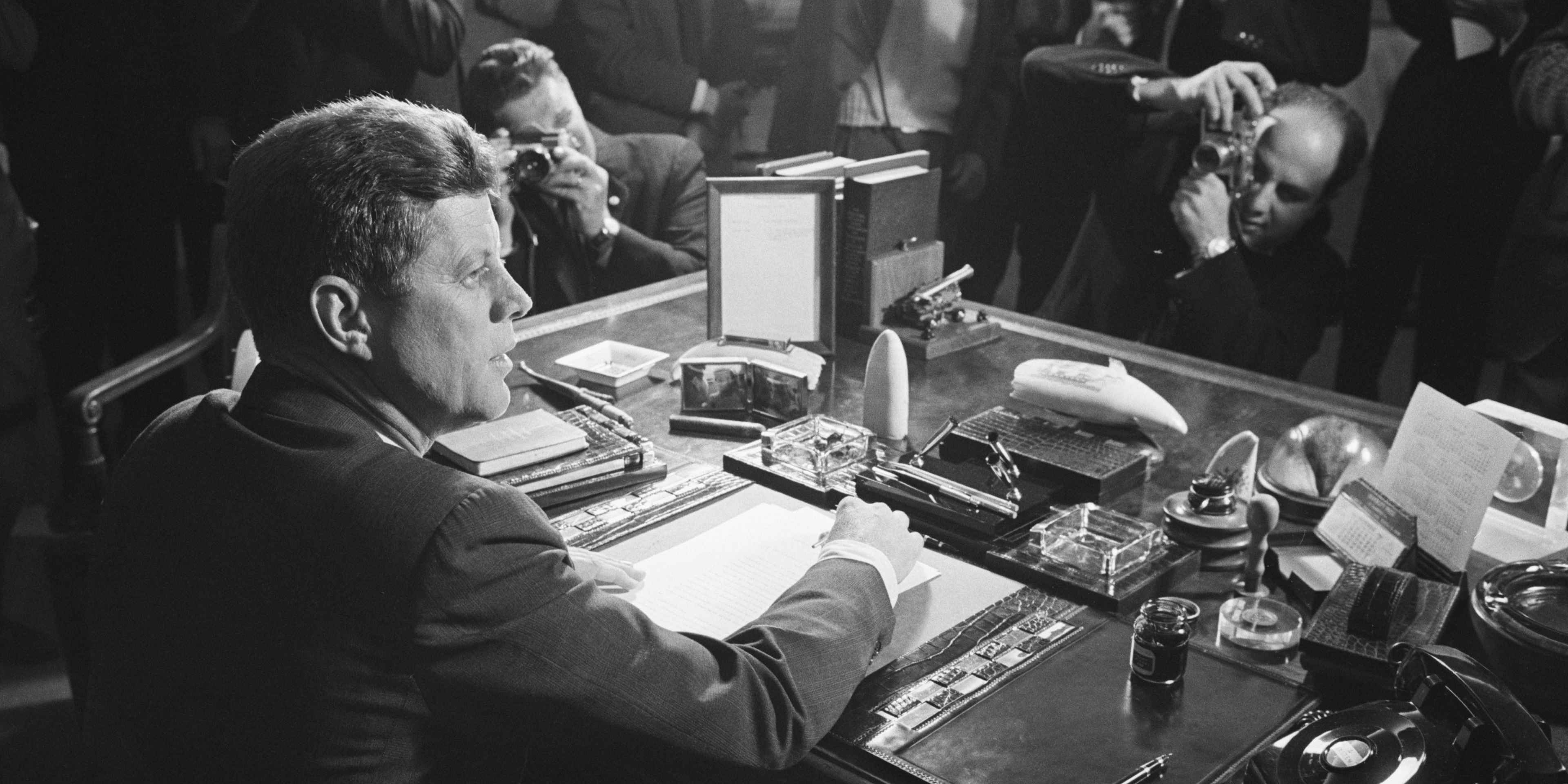 Reporters take pictures of President Kennedy behind his desk, after signing the arms embargo against Cuba. The embargo effectively quarantined Cuba.